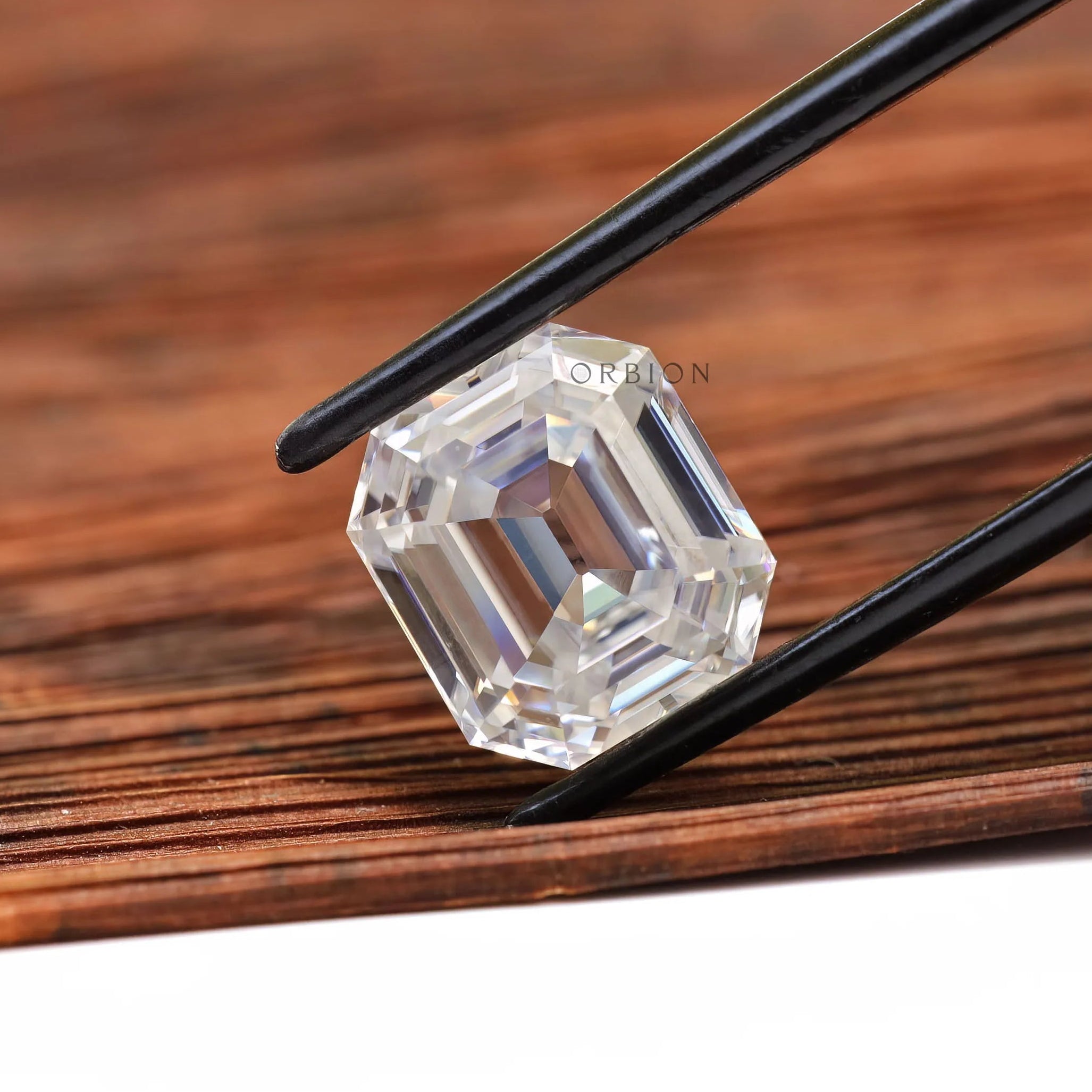 Emerald step cut loose moissanite held in tweezers on wood
