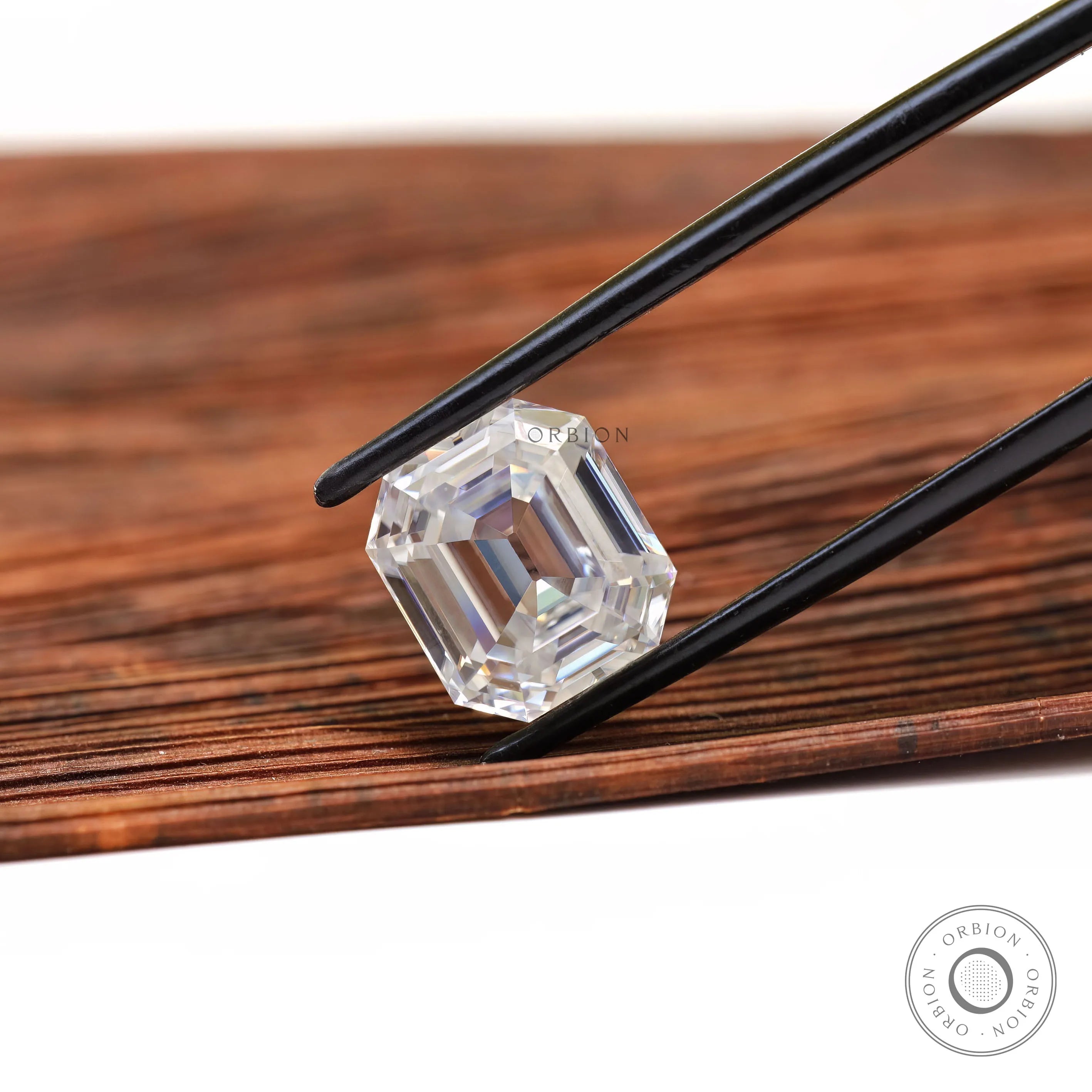 Emerald step cut loose moissanite held in tweezers on wood