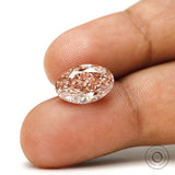 Intense pink oval lab diamond shown on fingertip closeup