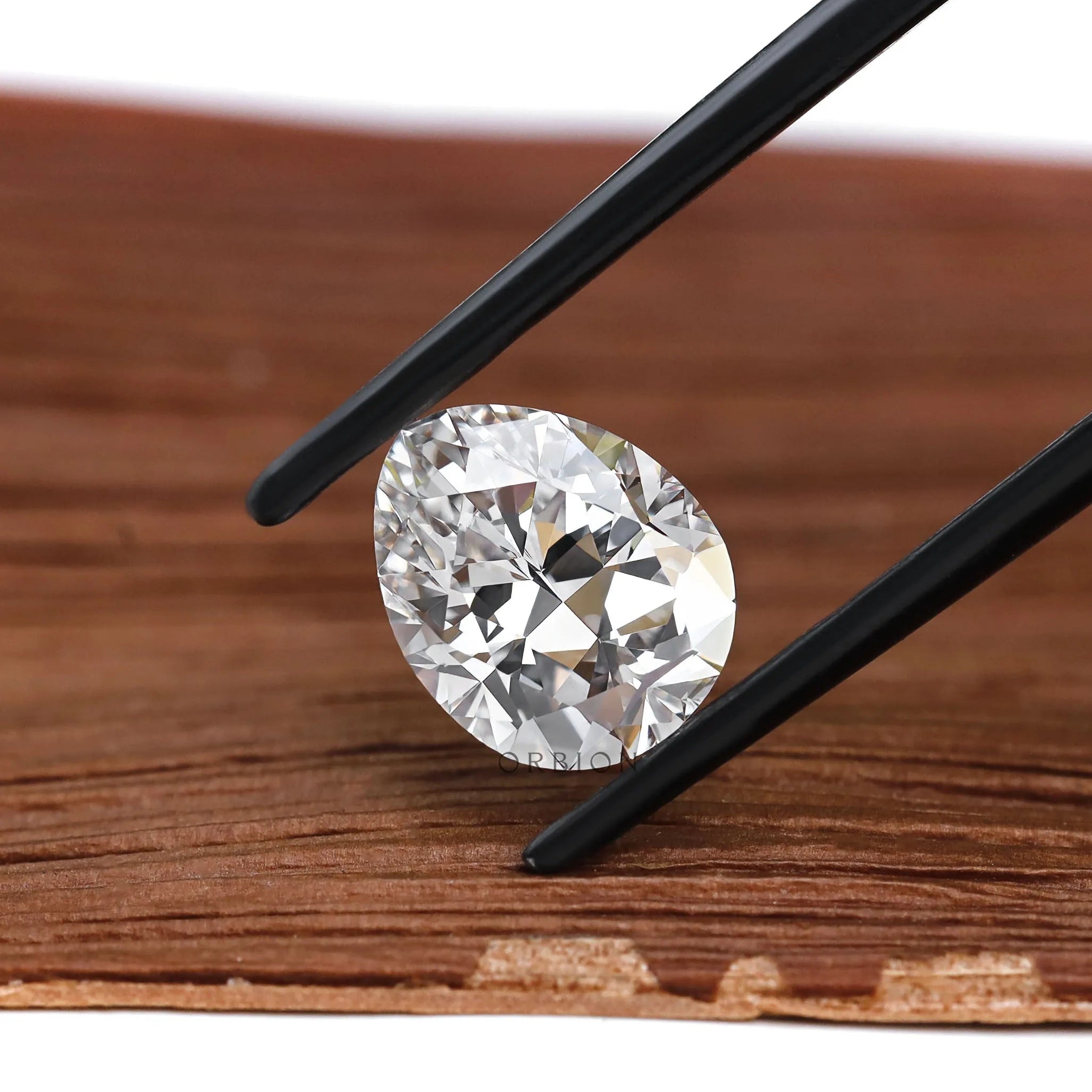 Pear brilliant cut lab diamond held above wooden surface