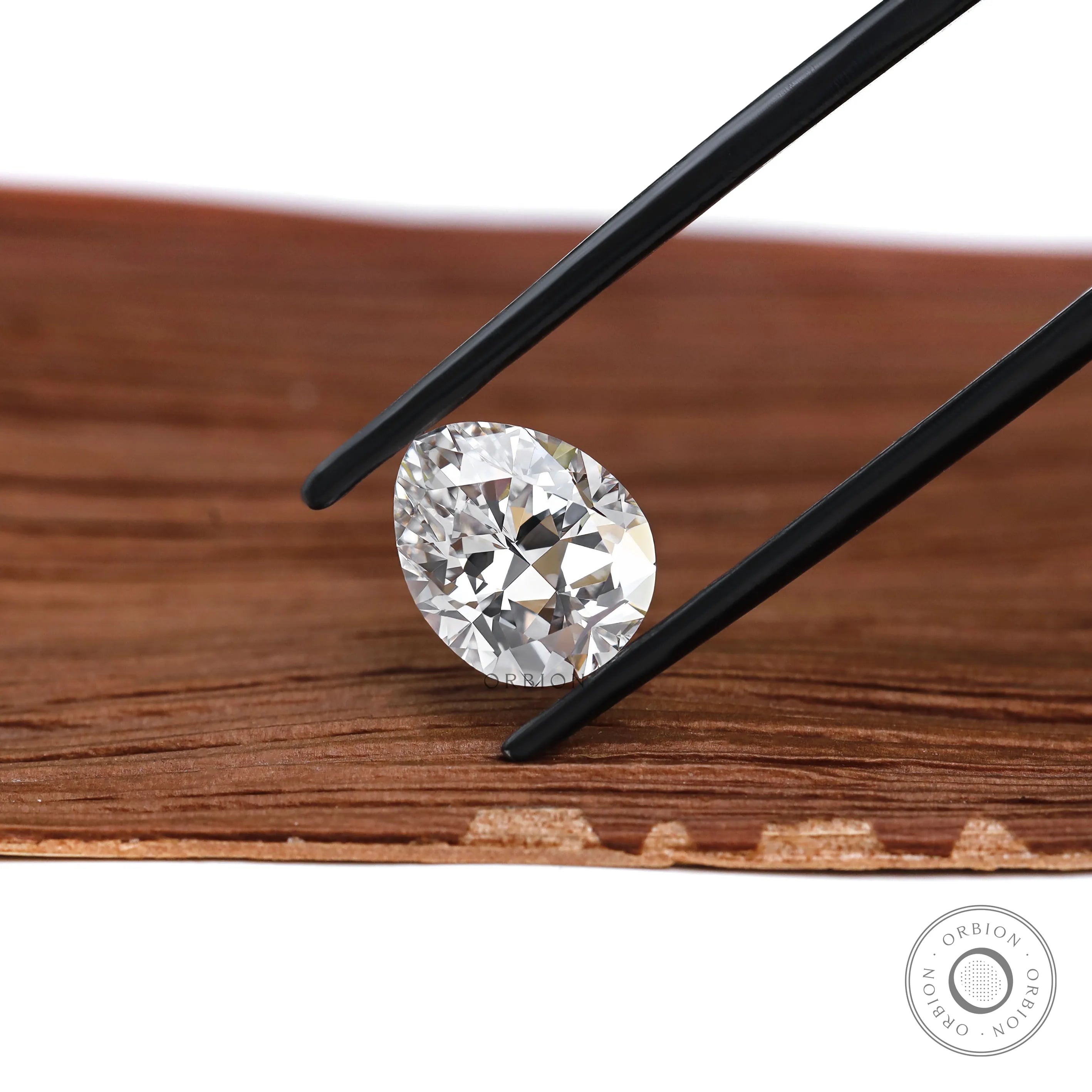 Pear brilliant cut lab diamond held above wooden surface