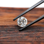 Round brilliant loose lab diamond in tweezers on wood