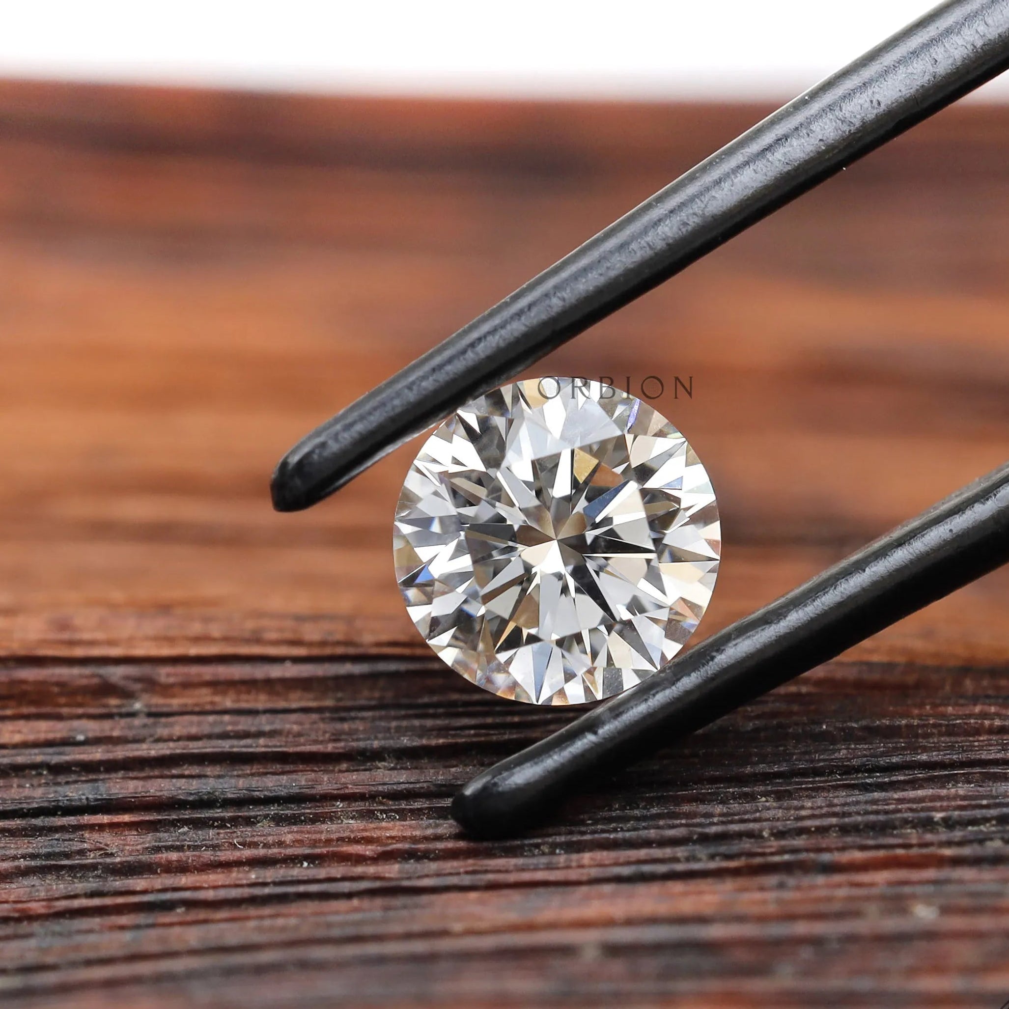 Round brilliant loose lab diamond in tweezers on wood