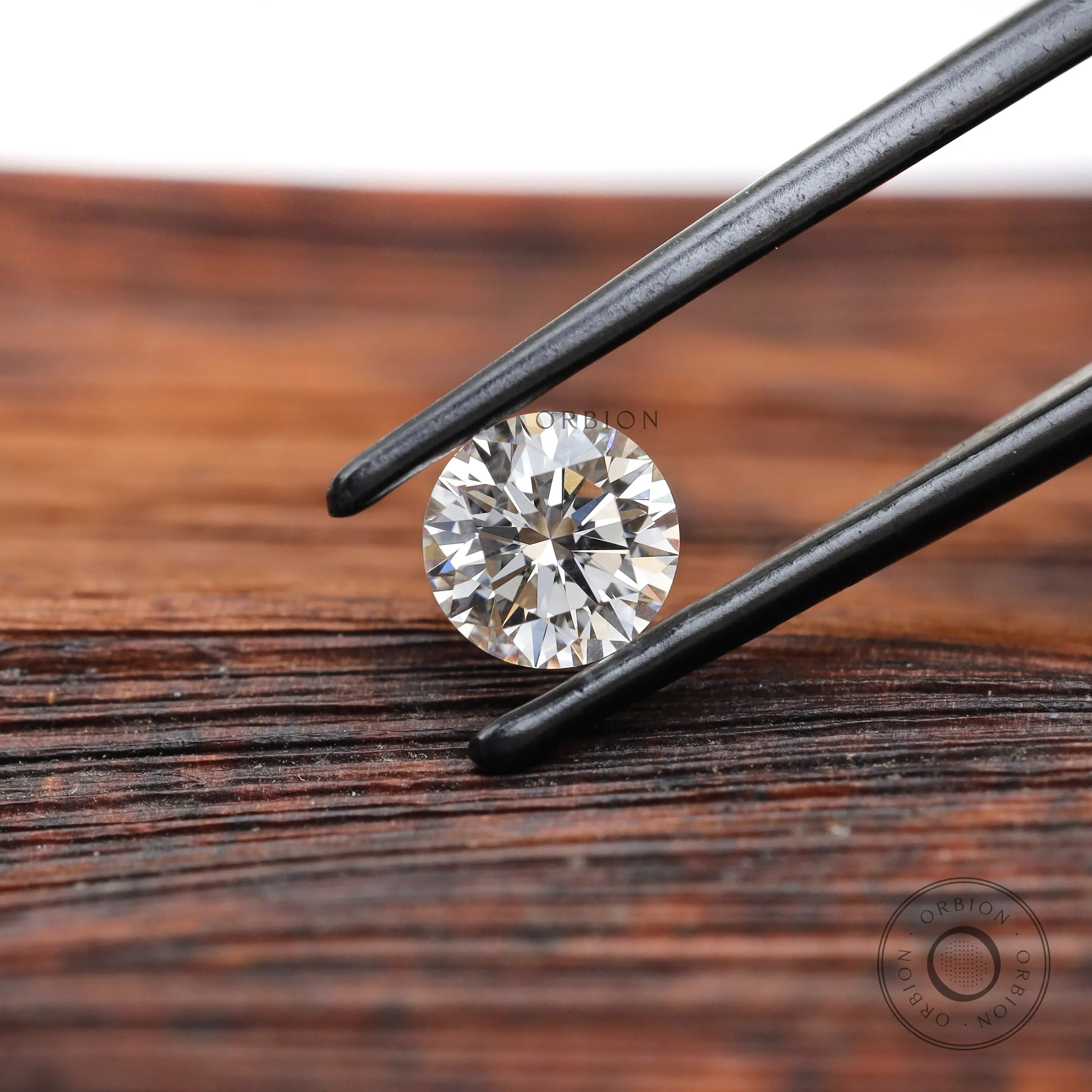 Round brilliant loose lab diamond in tweezers on wood