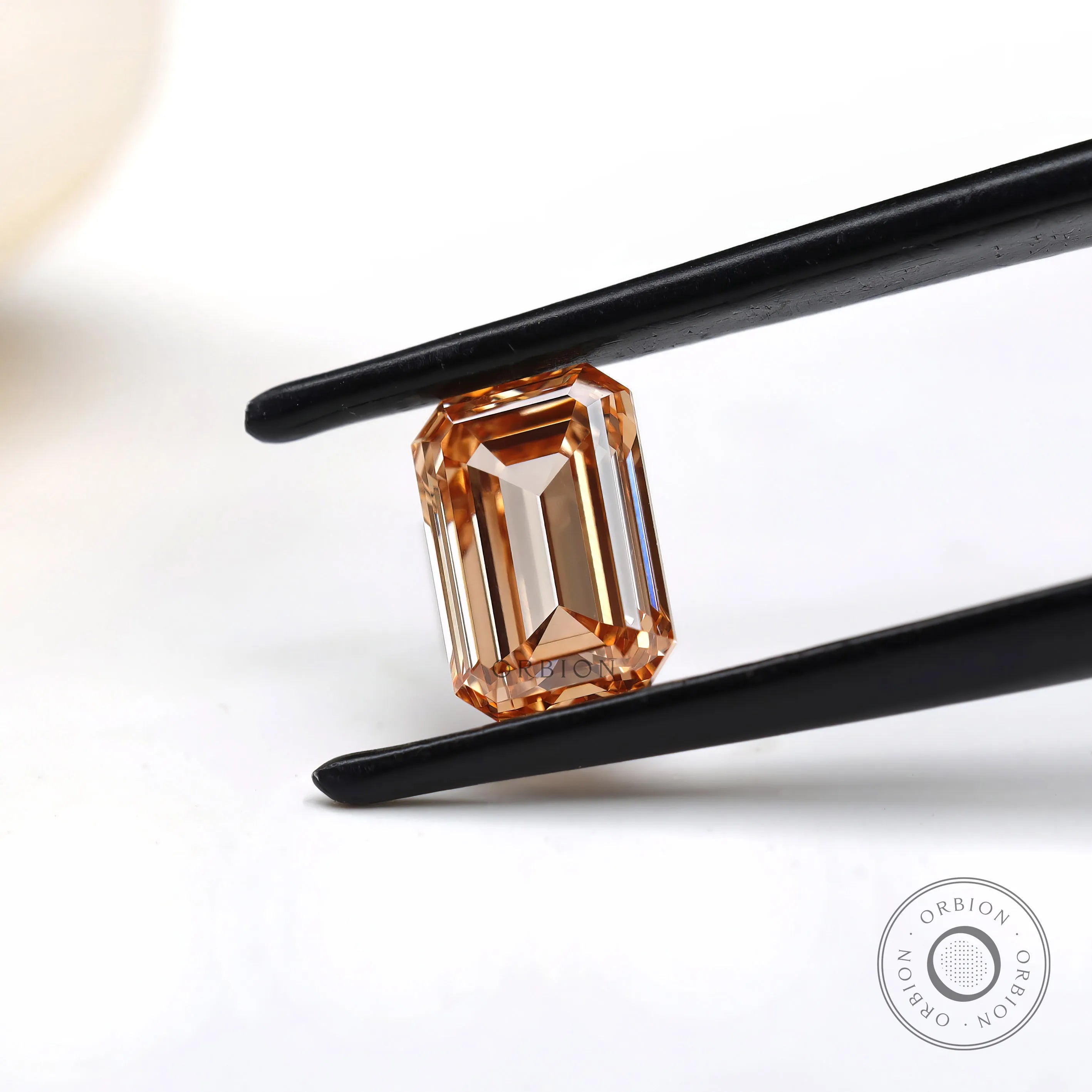 Fancy orange emerald step cut lab diamond in tweezers