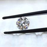 Round old European cut moissanite held in black tweezers