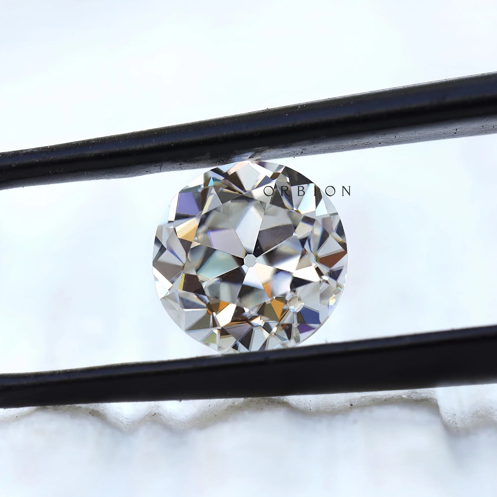Round old European cut moissanite held in black tweezers