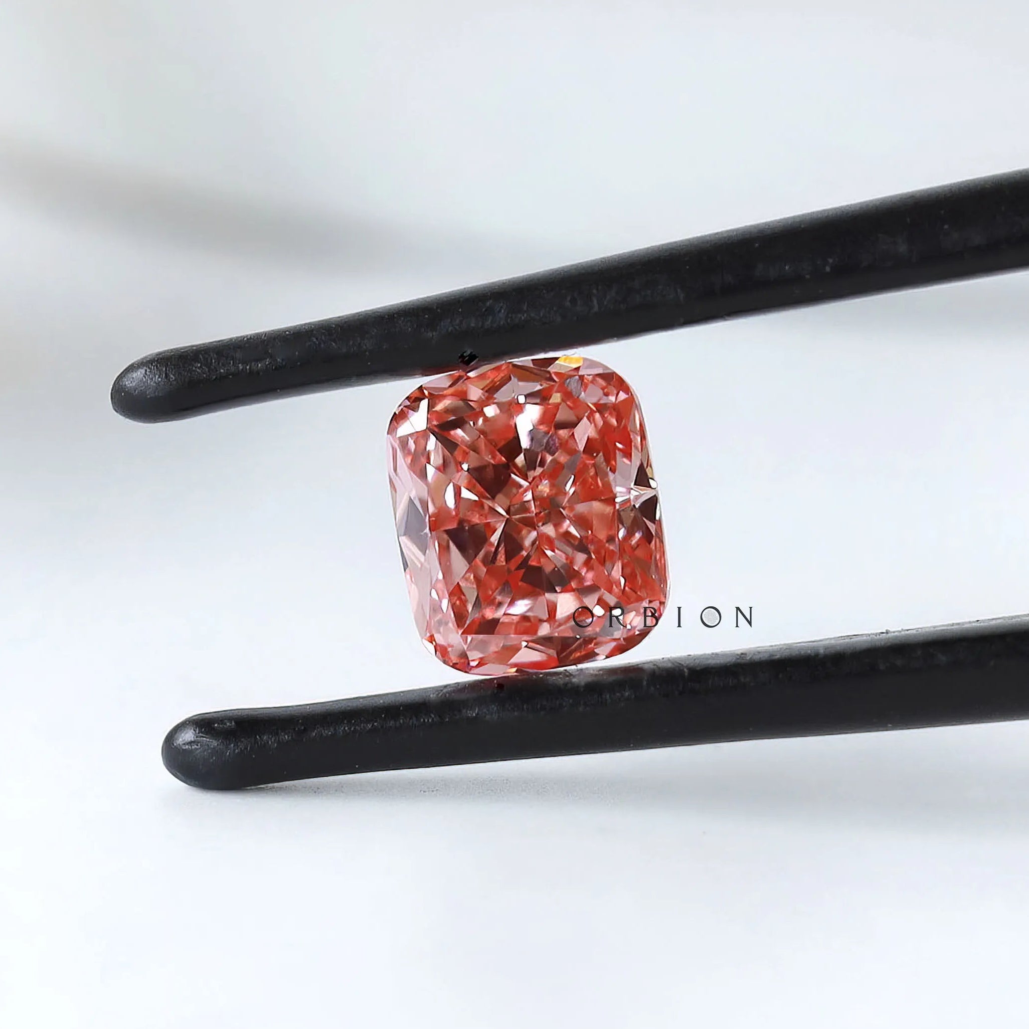 Fancy vivid pink cushion lab diamond held in black tweezers