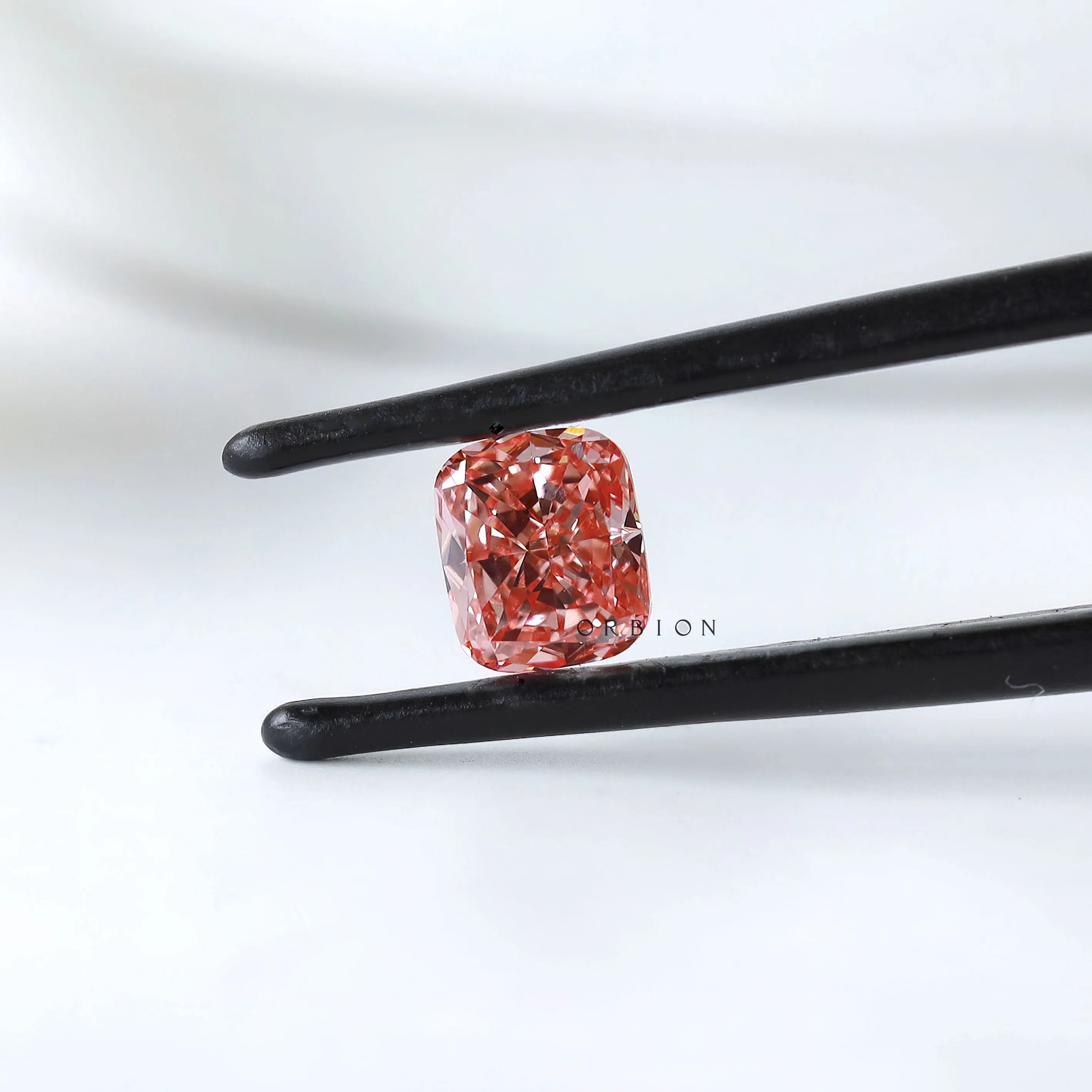 Fancy vivid pink cushion lab diamond held in black tweezers
