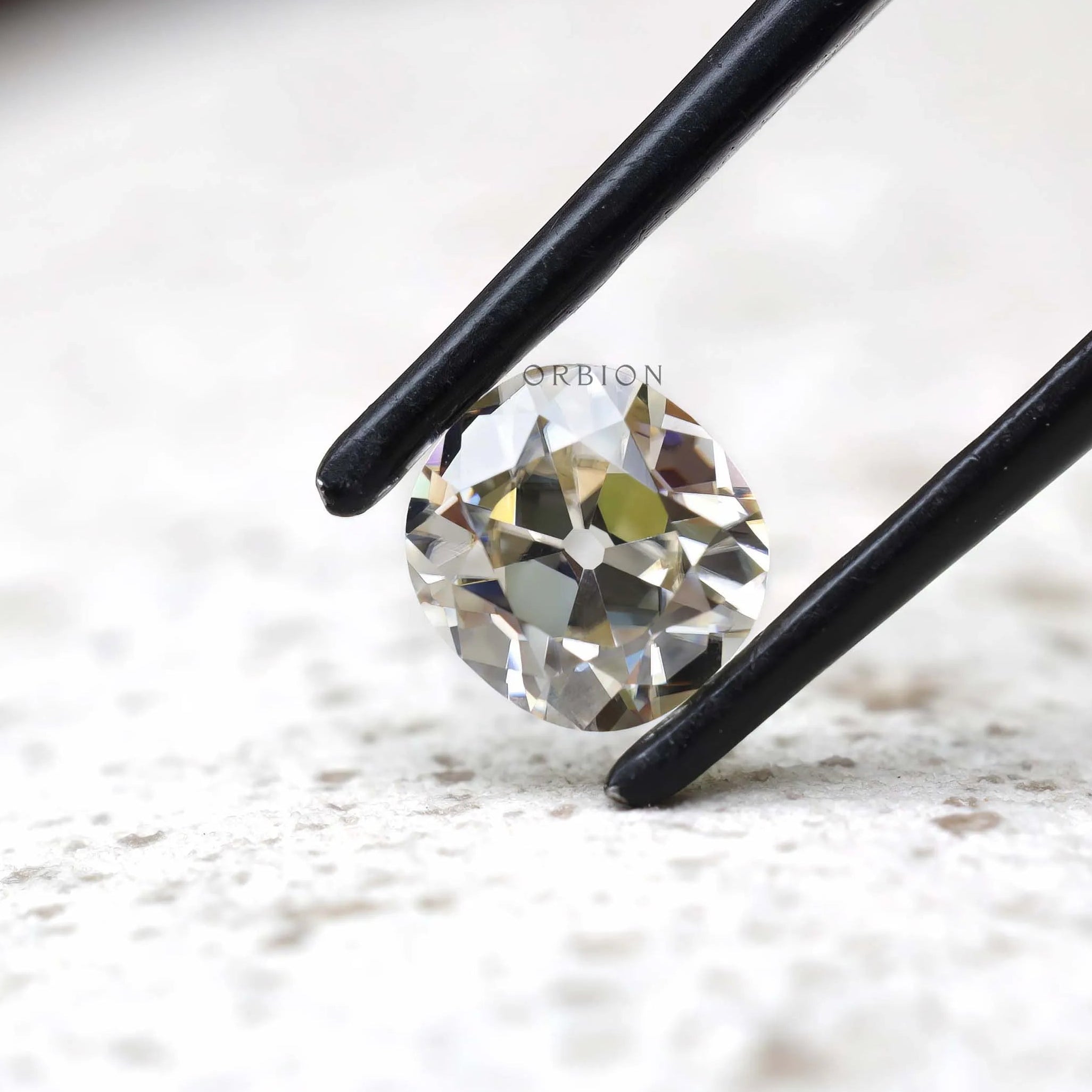 Elongated cushion old mine cut moissanite in tweezers angled view