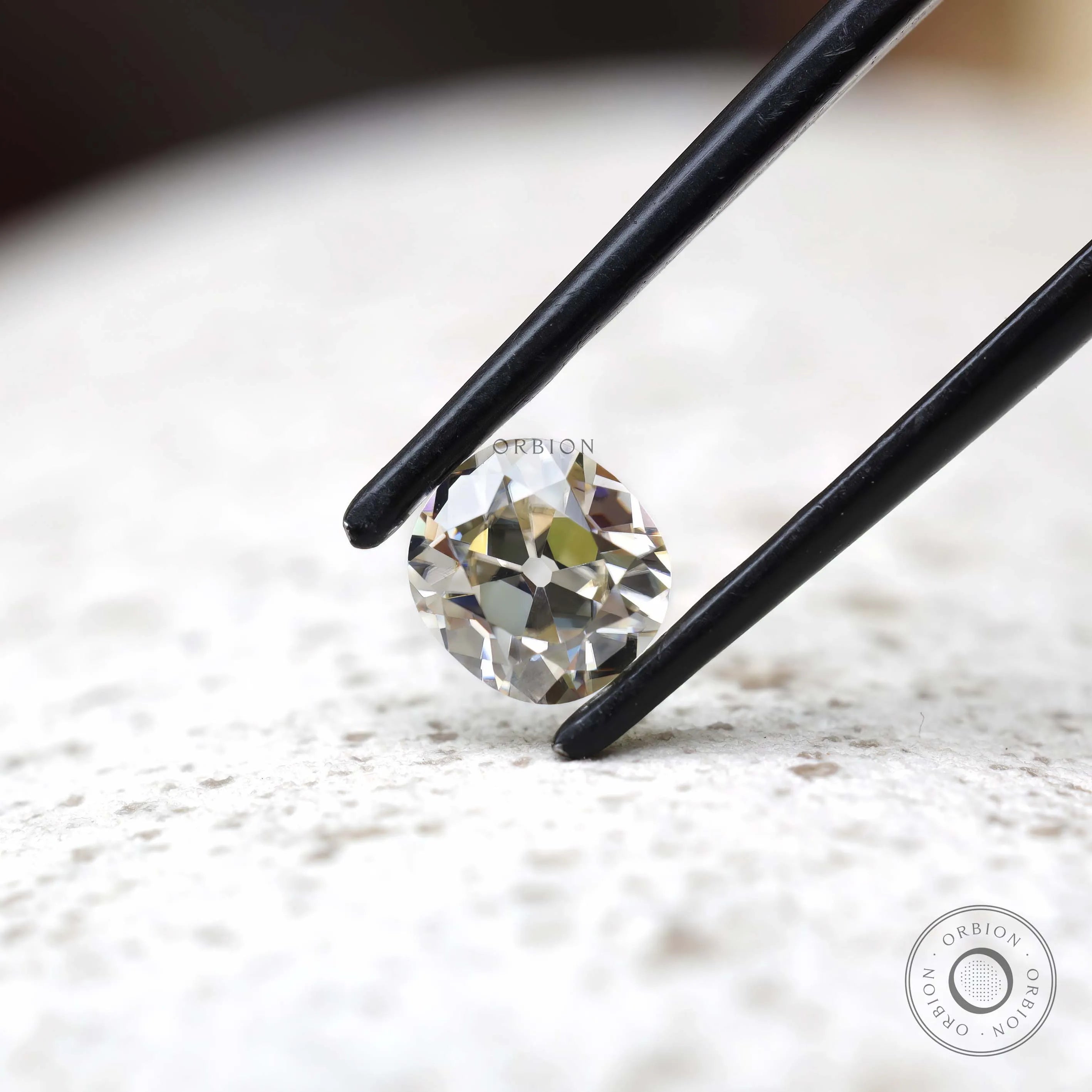 Elongated cushion old mine cut moissanite in tweezers angled view