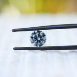 Round intense blue lab diamond held in black tweezers