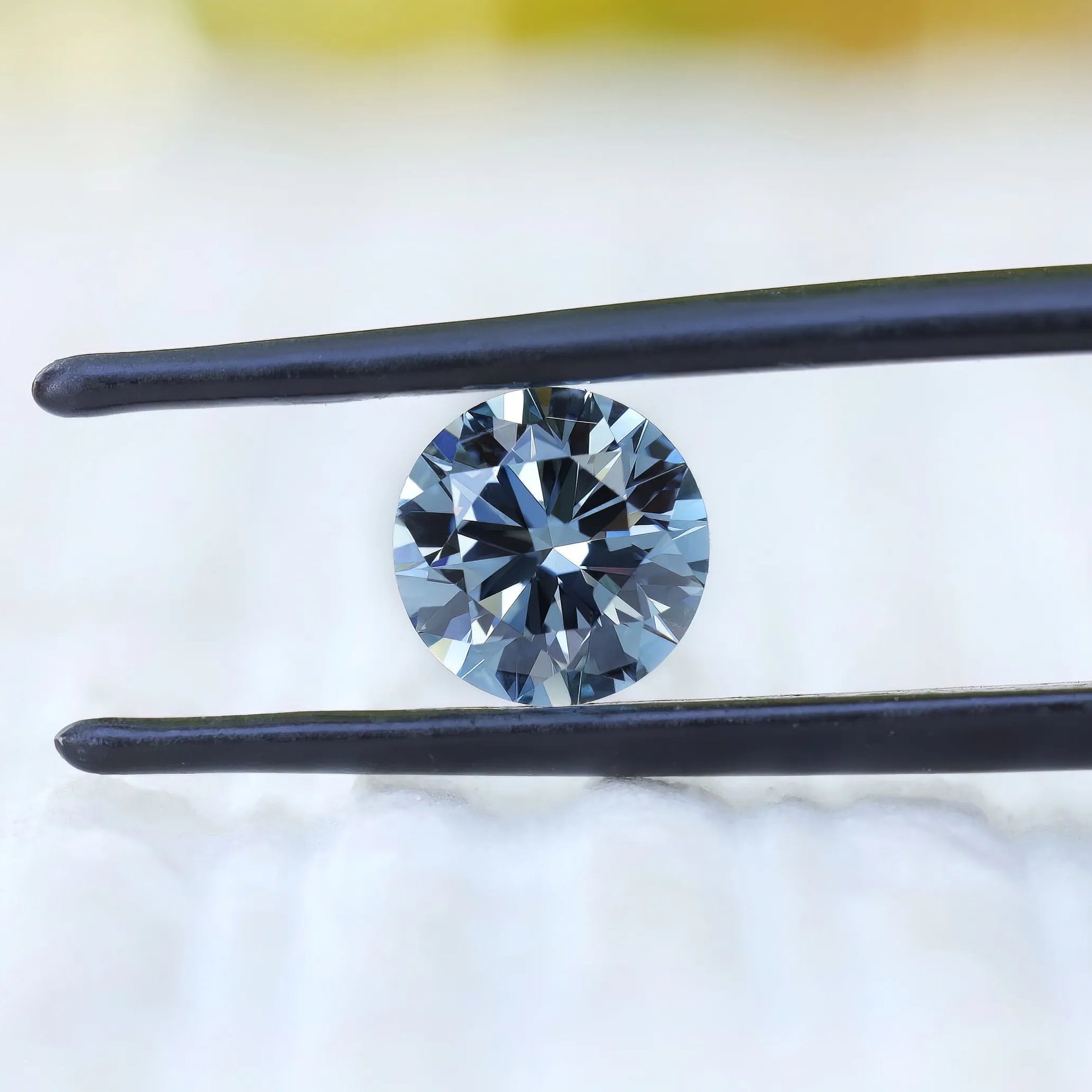 Round intense blue lab diamond held in black tweezers