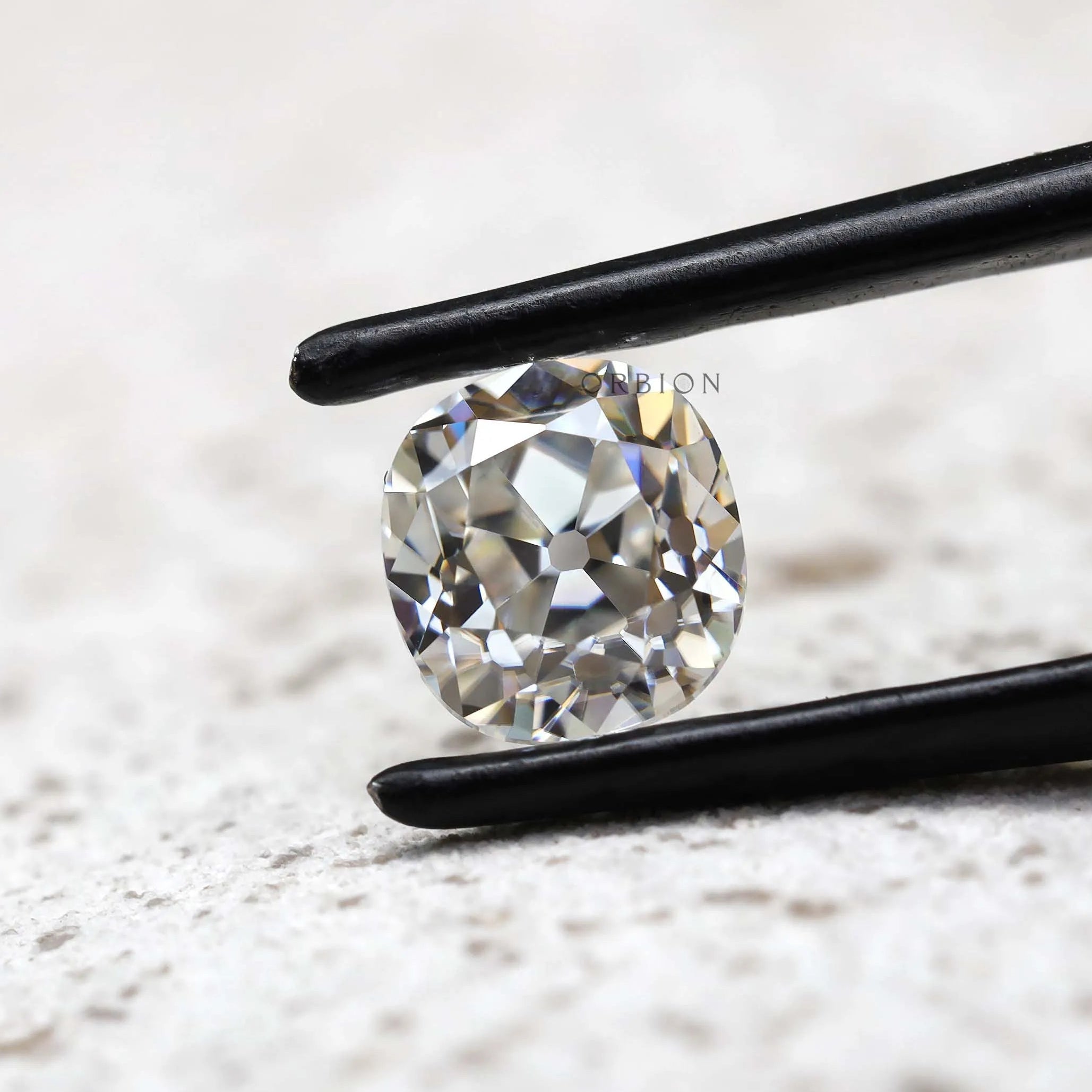 Elongated cushion old mine cut moissanite in tweezer close-up
