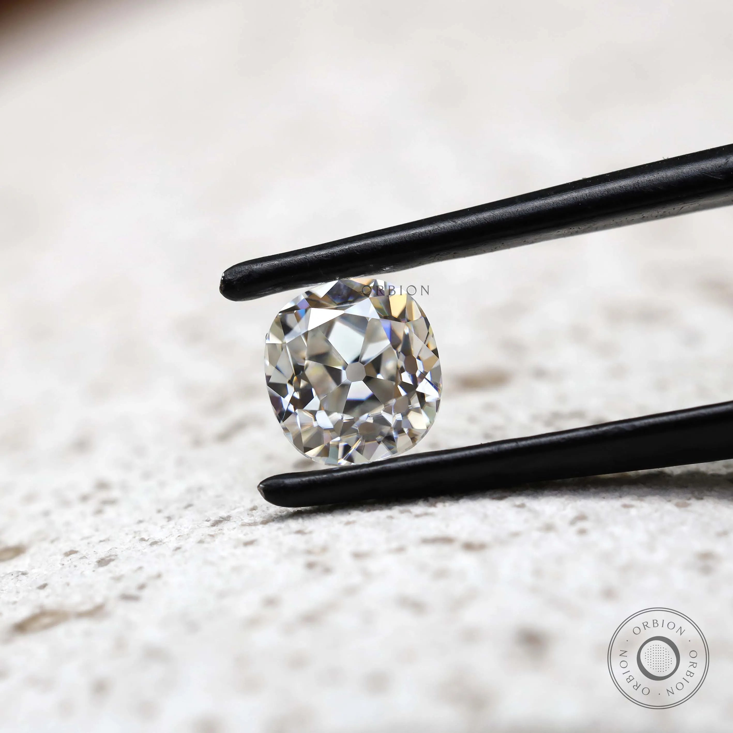 Elongated cushion old mine cut moissanite in tweezer close-up