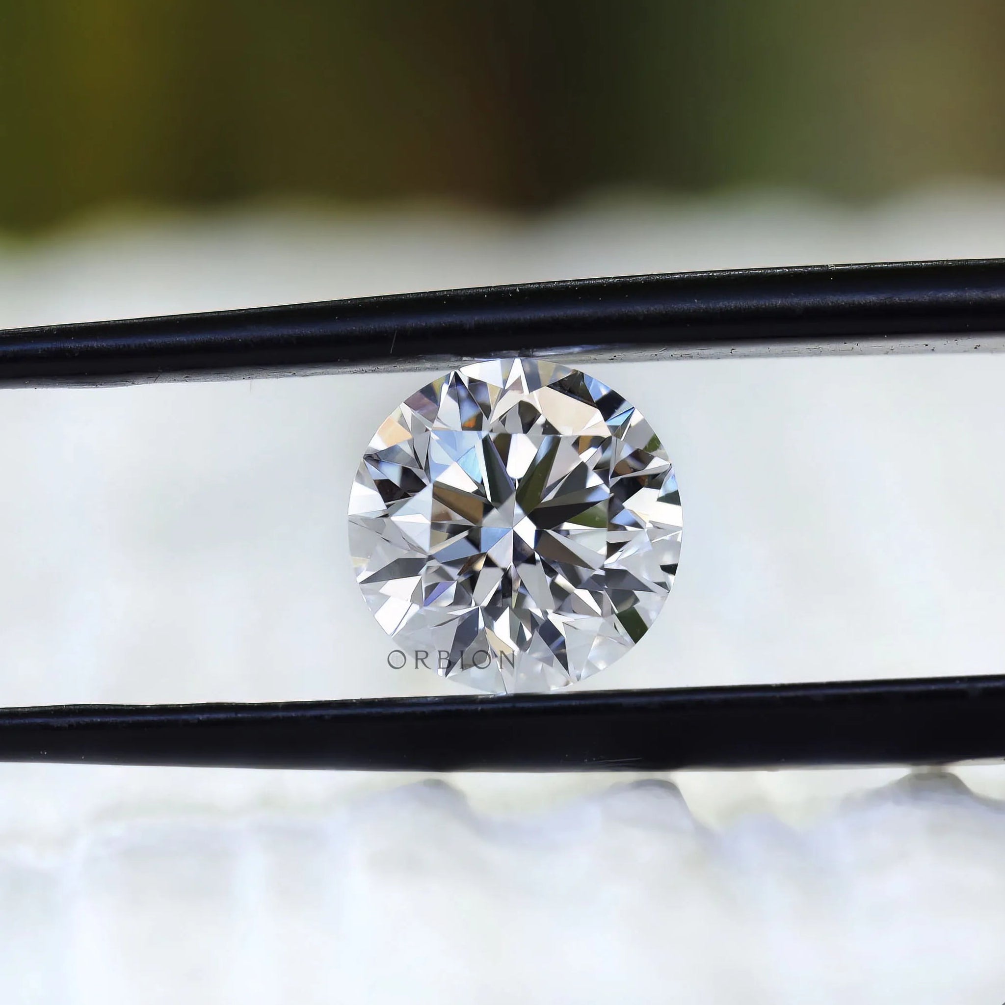 Round colorless lab diamond displayed between black tweezers