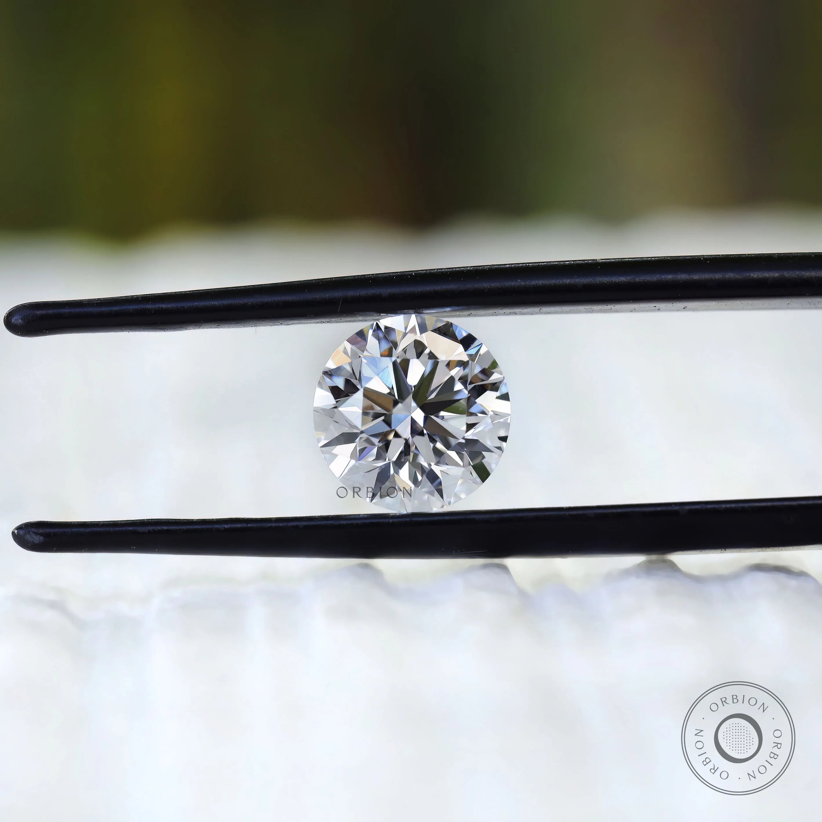 Round colorless lab diamond displayed between black tweezers