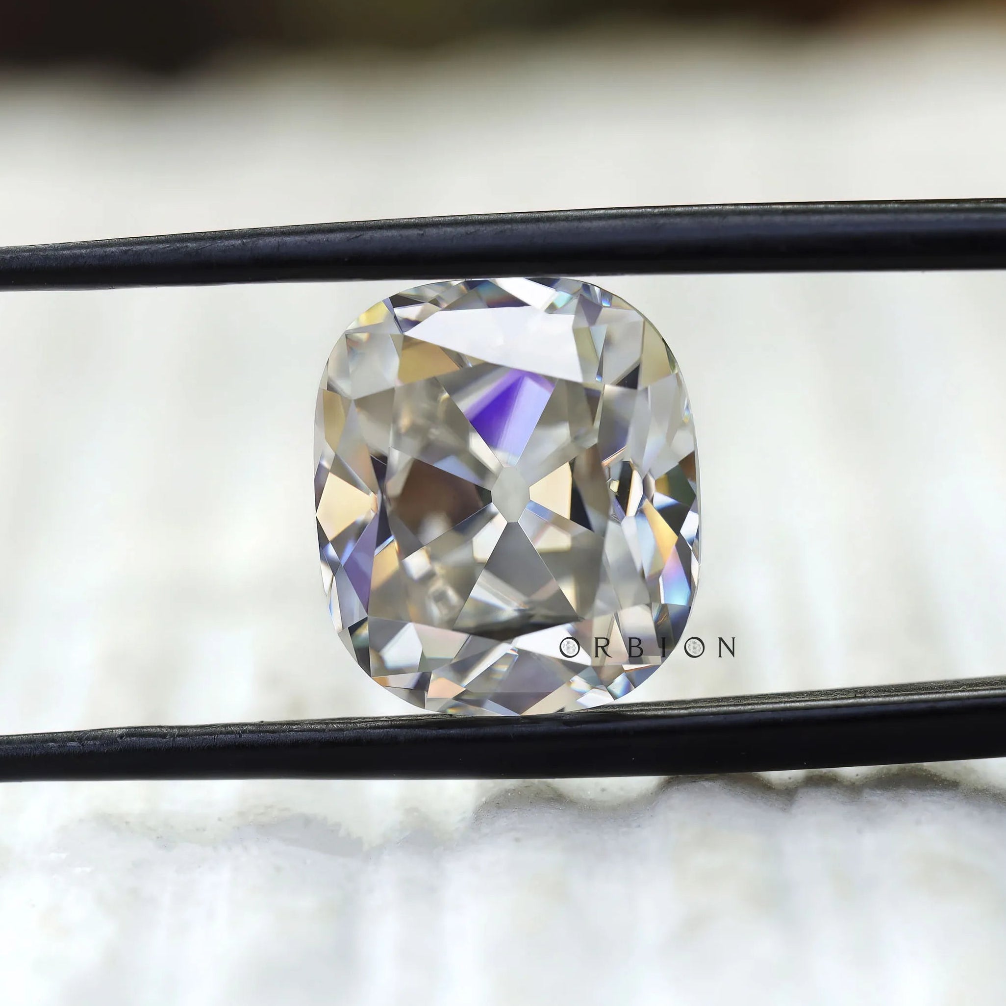 Cushion old mine cut moissanite held in tweezers