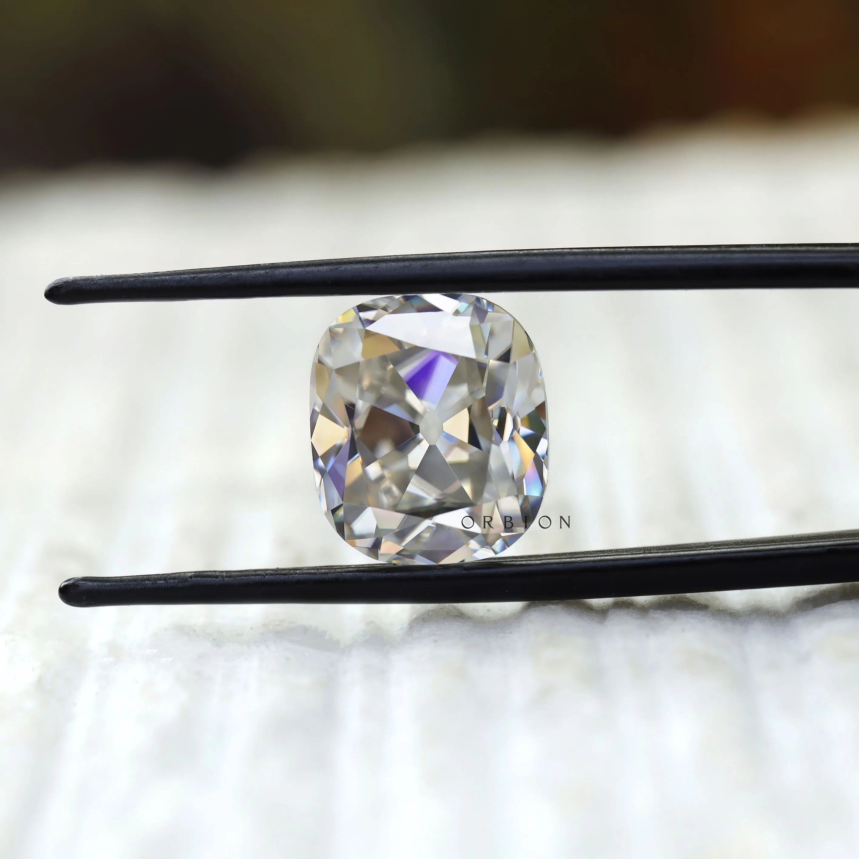 Cushion old mine cut moissanite held in tweezers