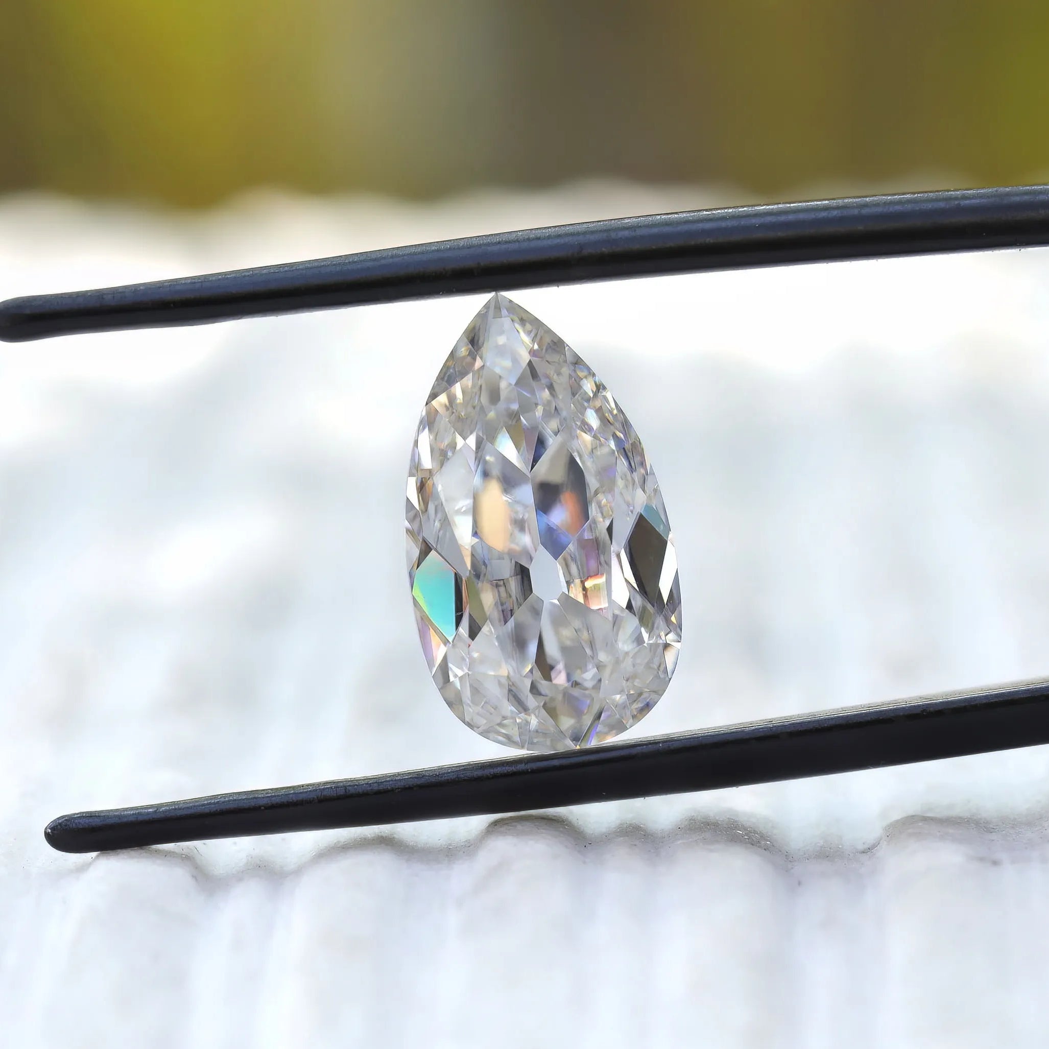 Pear old mine cut moissanite held upright in tweezers