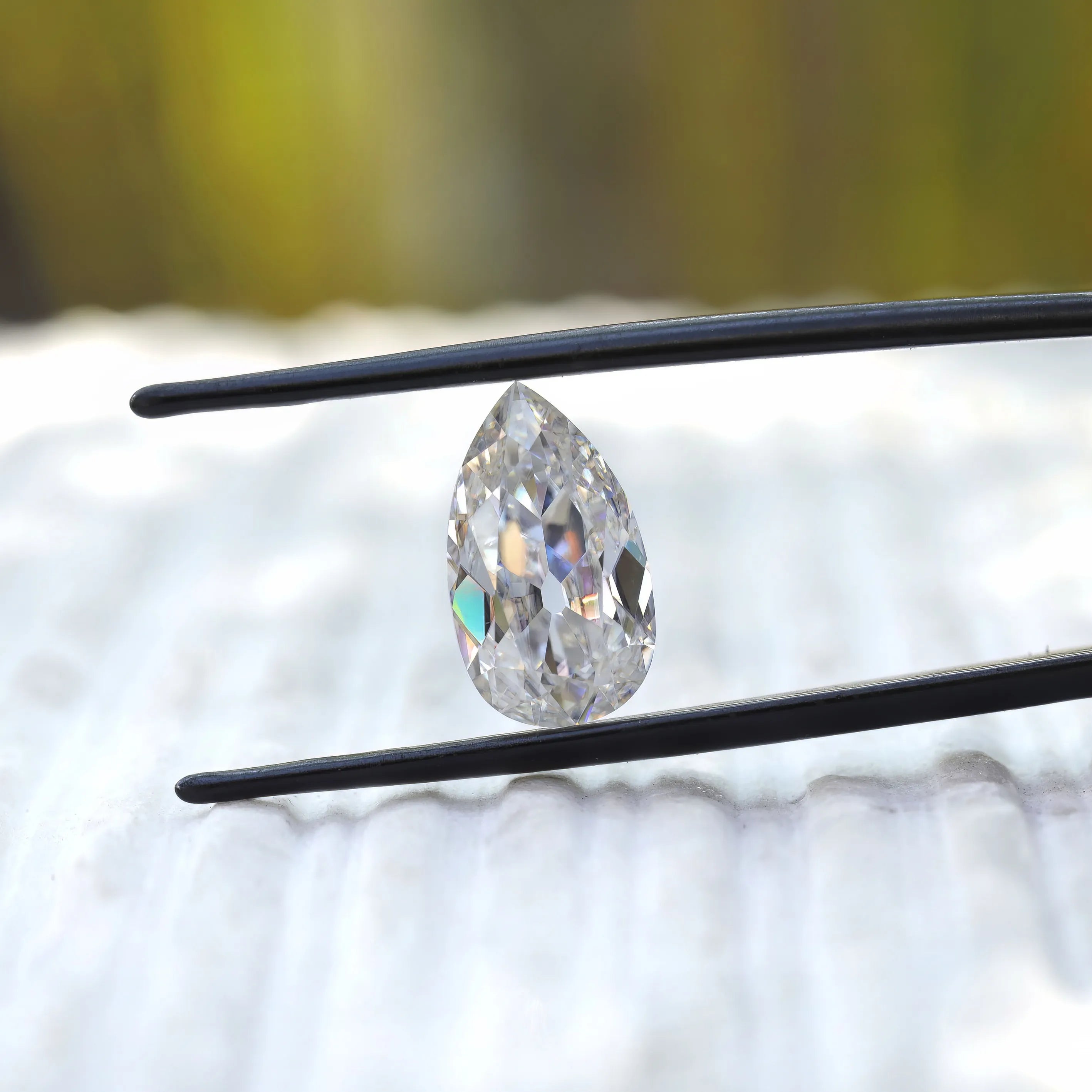 Pear old mine cut moissanite held upright in tweezers