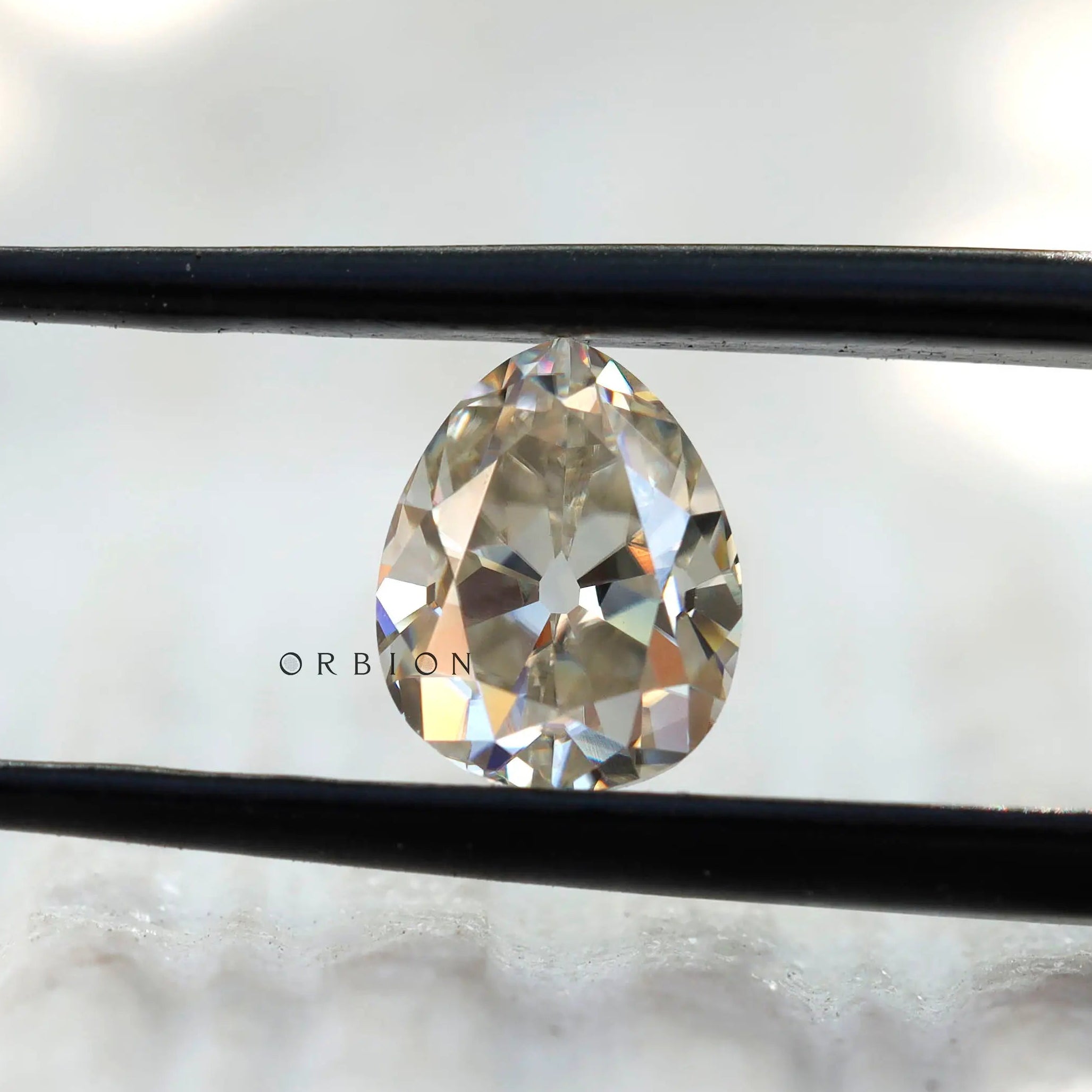 Old Mine Cut Off White Pear Moissanite Loose Stone in tweezers