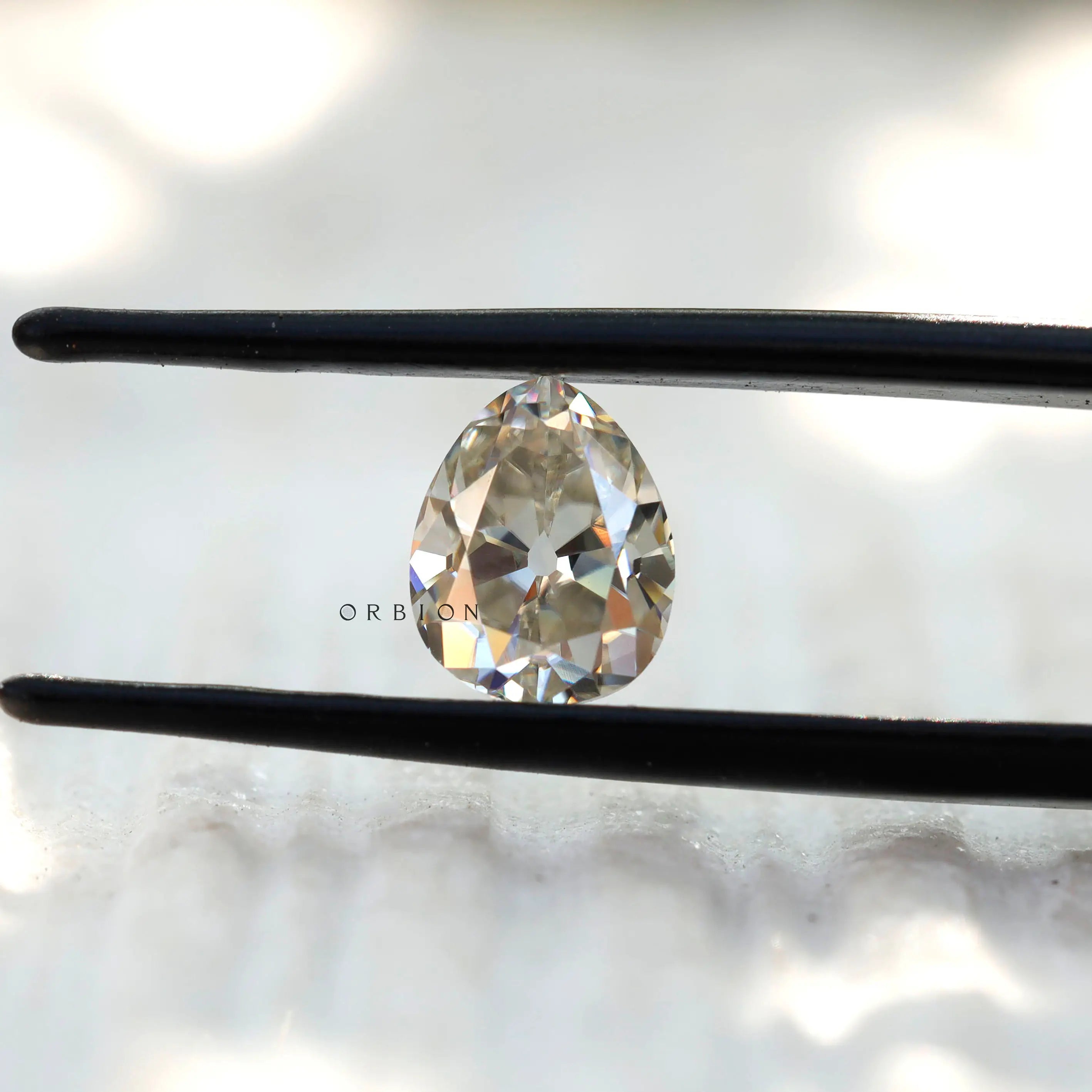 Old Mine Cut Off White Pear Moissanite Loose Stone in tweezers