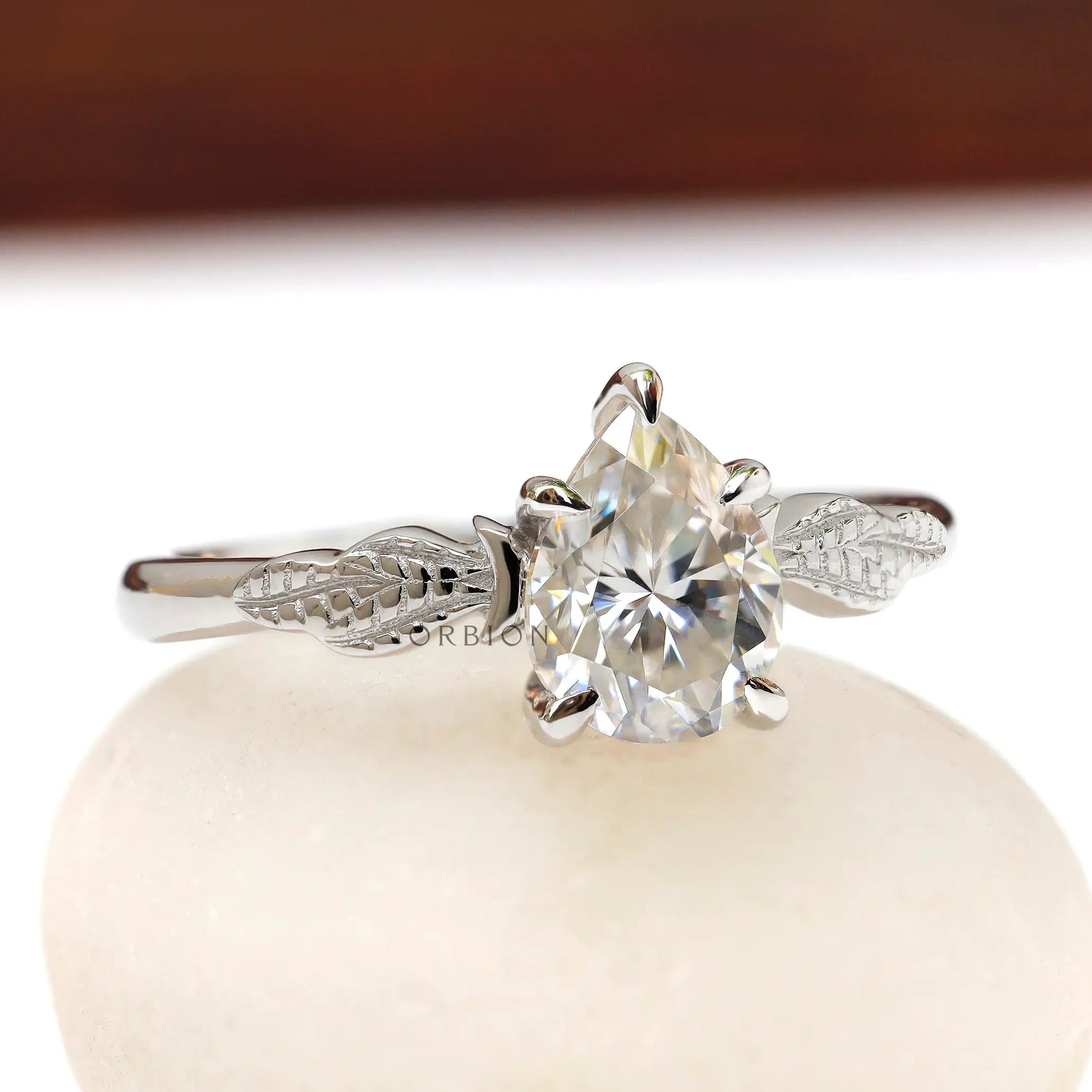 Angled view of pear Moissanite engagement ring with leaf details
