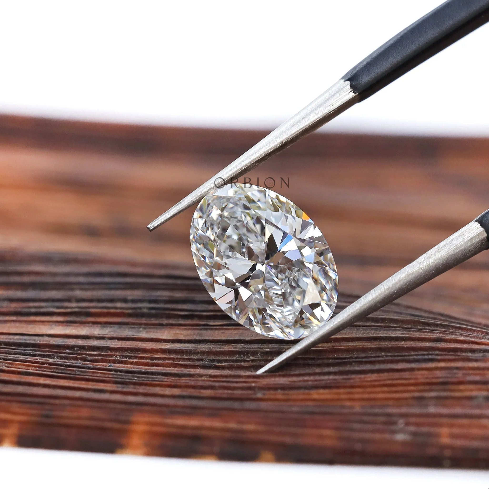 Oval brilliant cut lab diamond held with tweezers on wood
