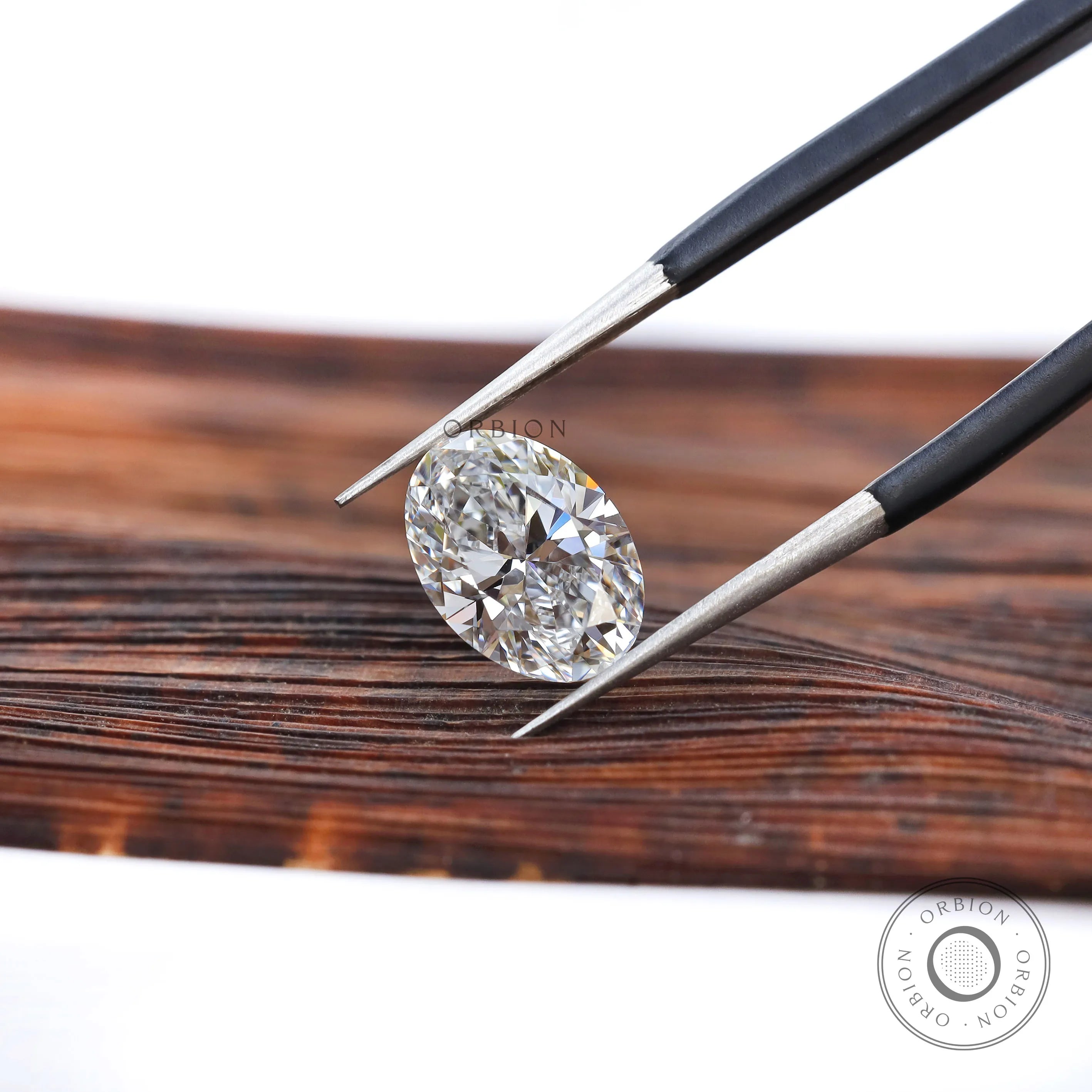 Oval brilliant cut lab diamond held with tweezers on wood