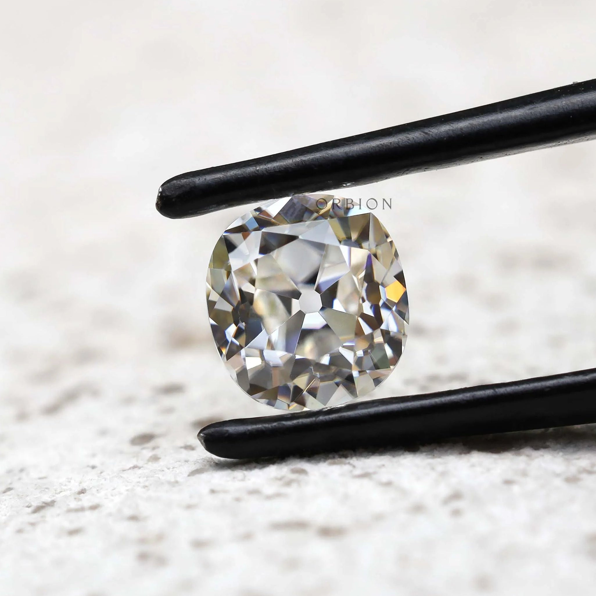 DEF elongated cushion loose moissanite shown in black tweezers