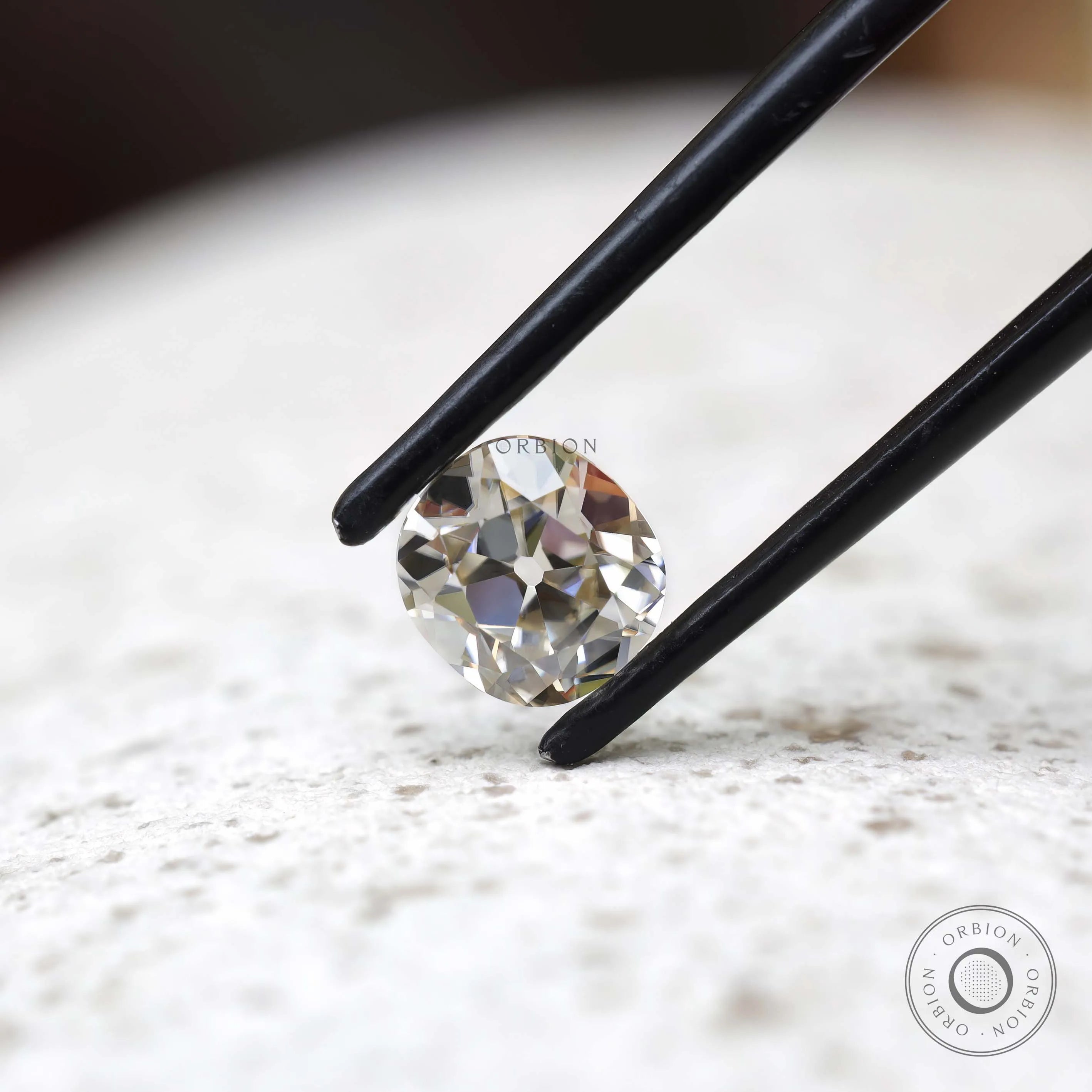 GHI elongated cushion moissanite held in black tweezers close-up