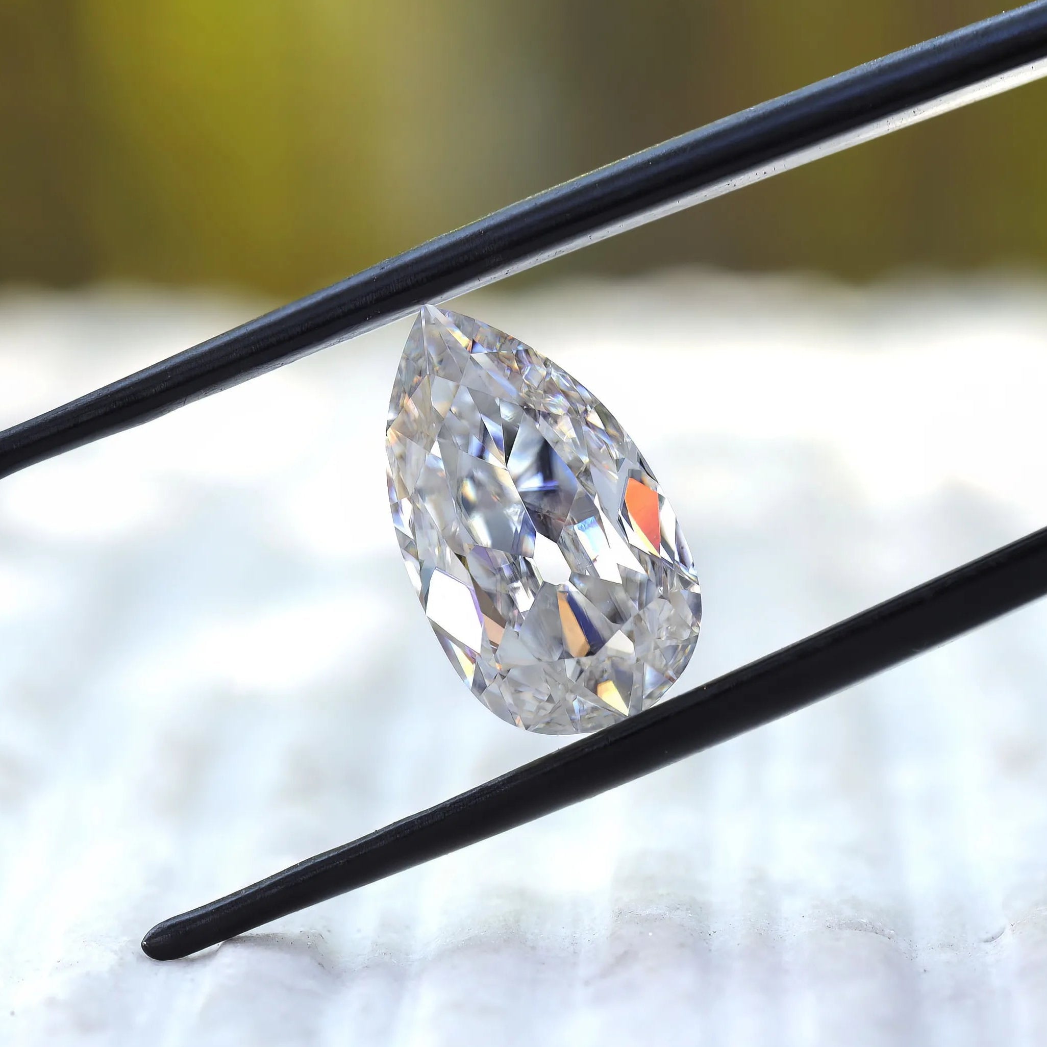 Angled pear old mine cut moissanite in black tweezers