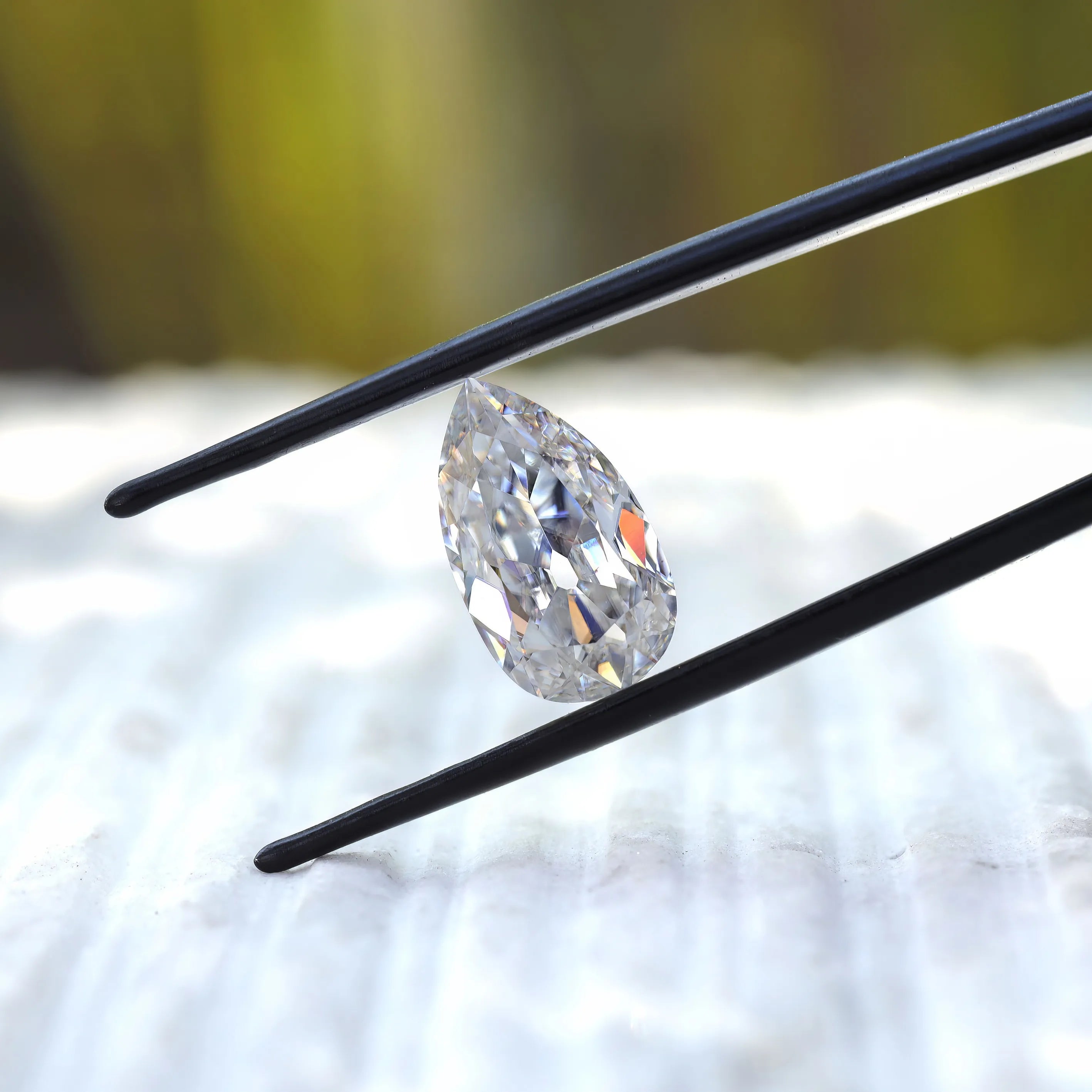 Angled pear old mine cut moissanite in black tweezers