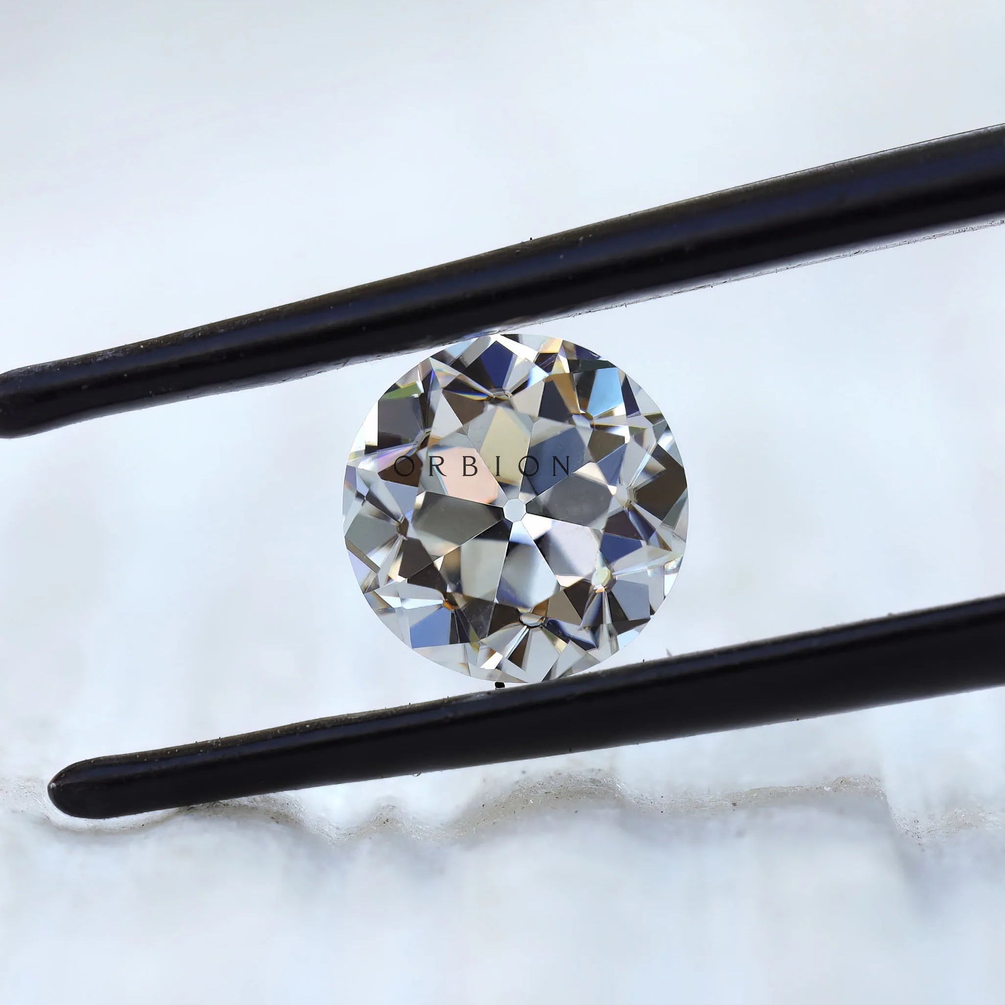DEF round moissanite showing antique faceting in tweezers