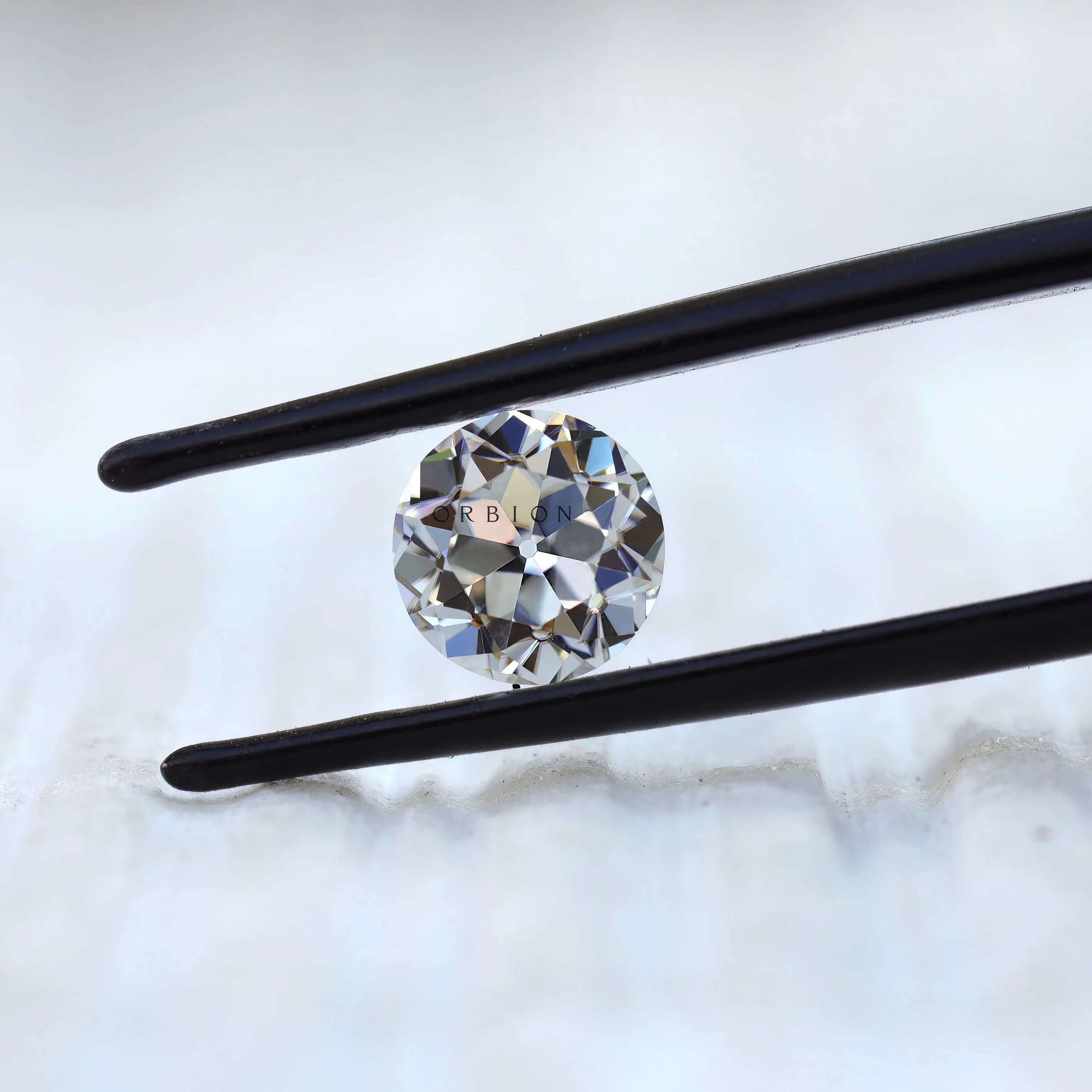 DEF round moissanite showing antique faceting in tweezers