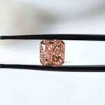 Fancy vivid pink radiant diamond held between black tweezers