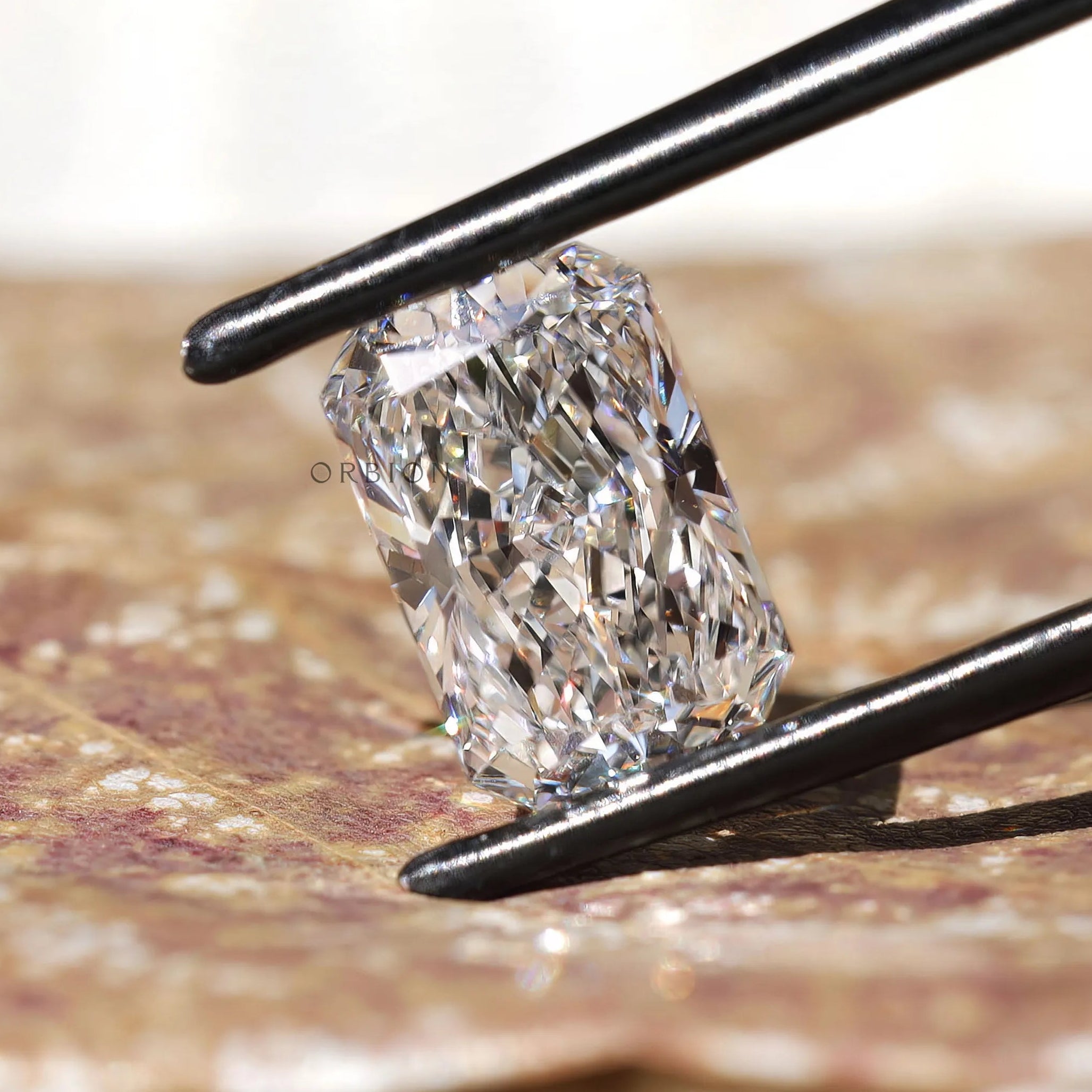 White radiant brilliant diamond held with black tweezers