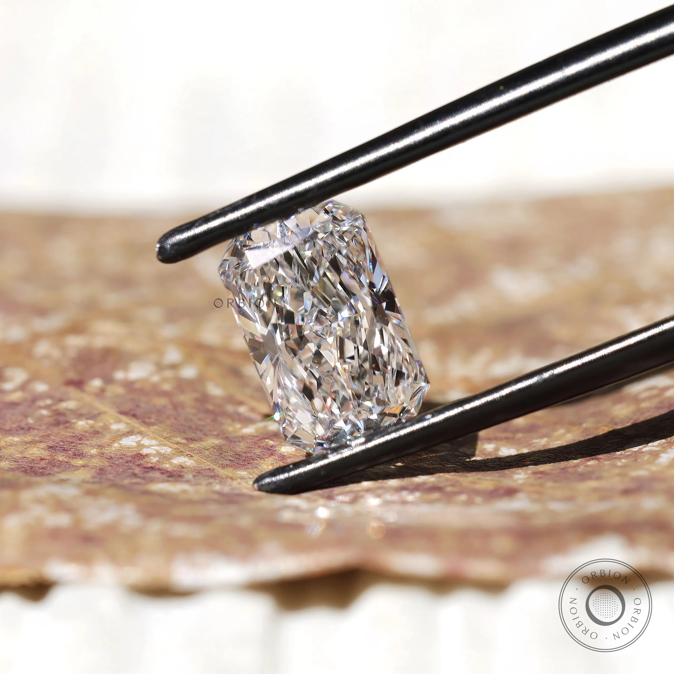 White radiant brilliant diamond held with black tweezers