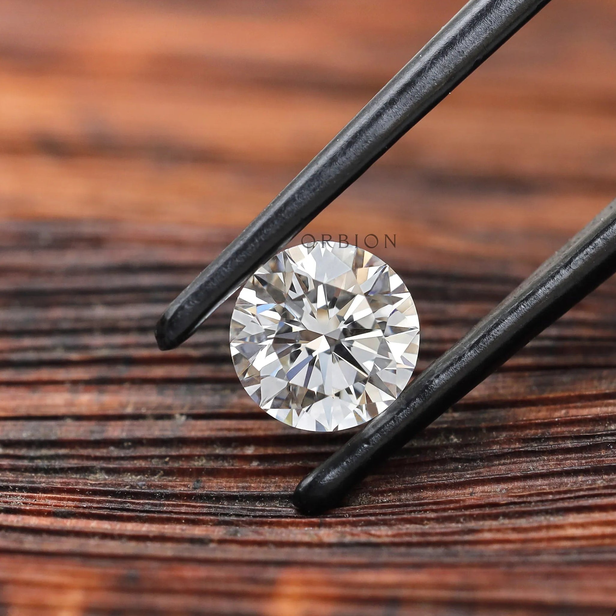Angled round brilliant loose diamond held in black tweezers