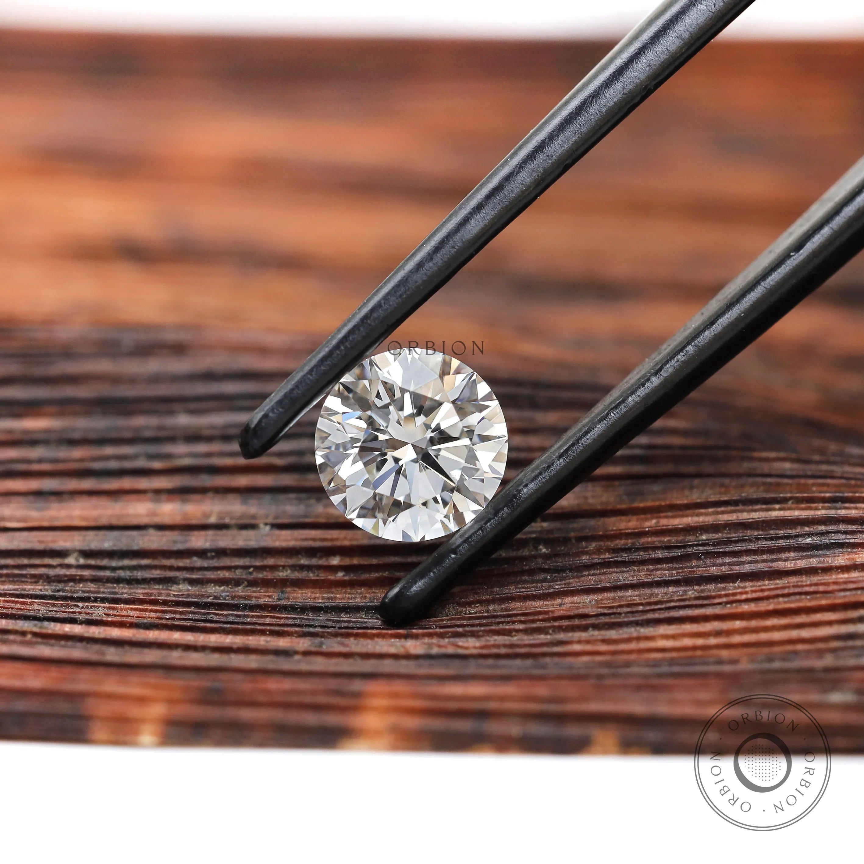 Angled round brilliant loose diamond held in black tweezers
