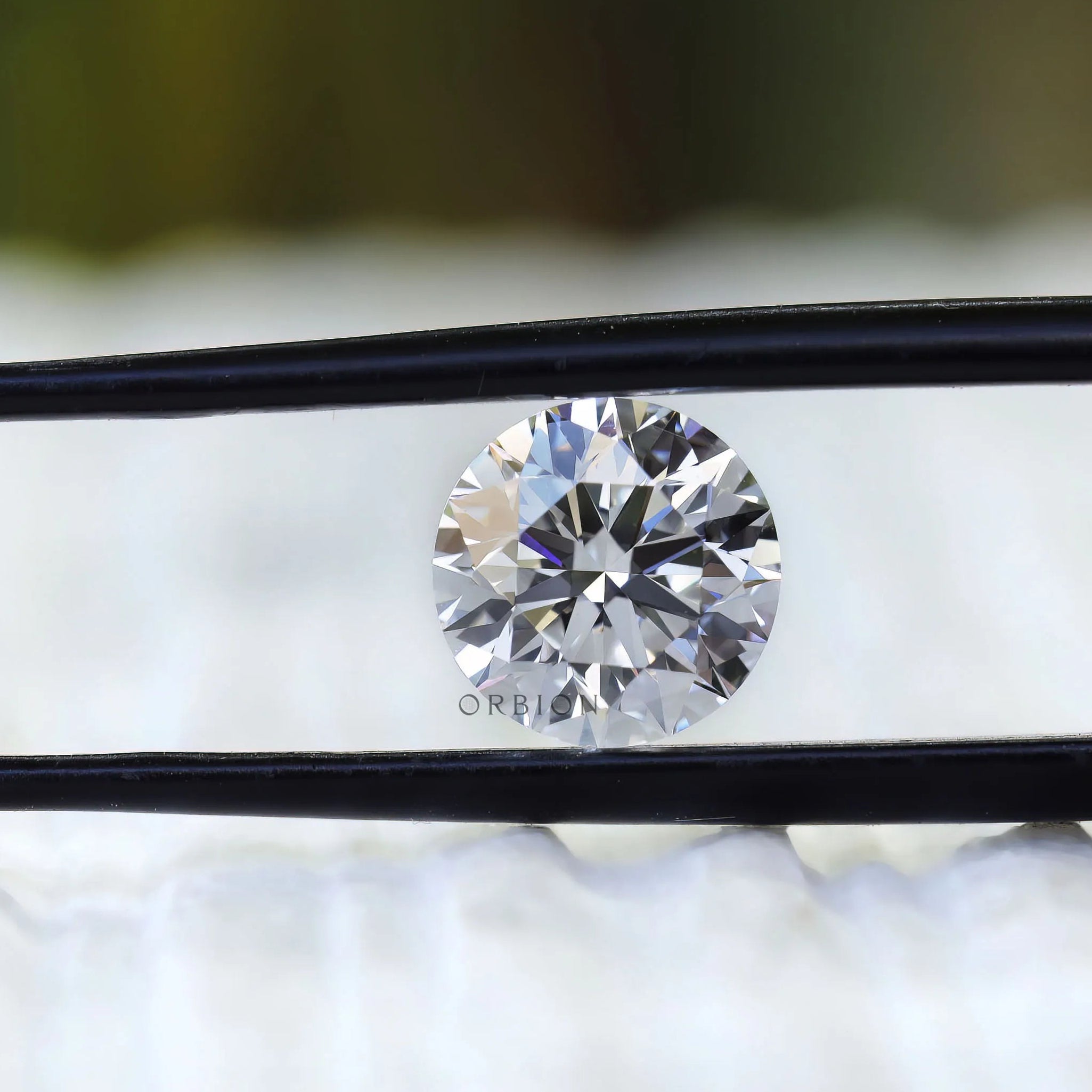 Round brilliant loose diamond angled between black tweezers