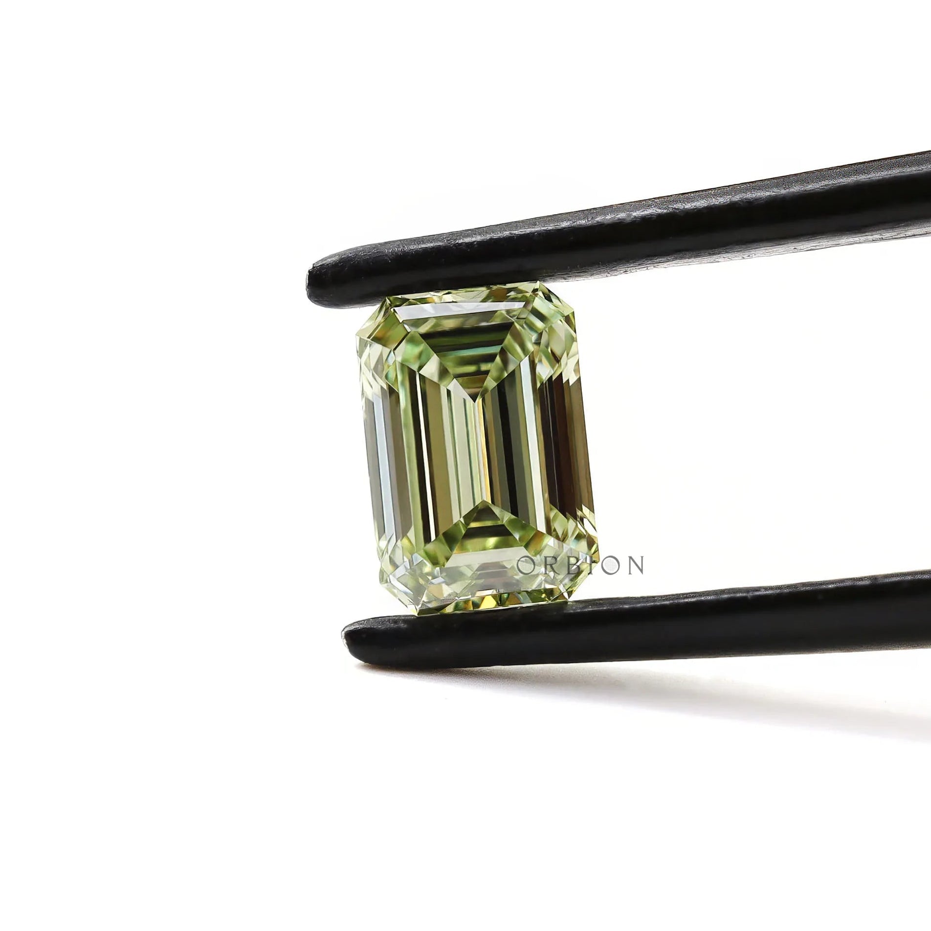 Fancy green emerald diamond held horizontally in tweezers