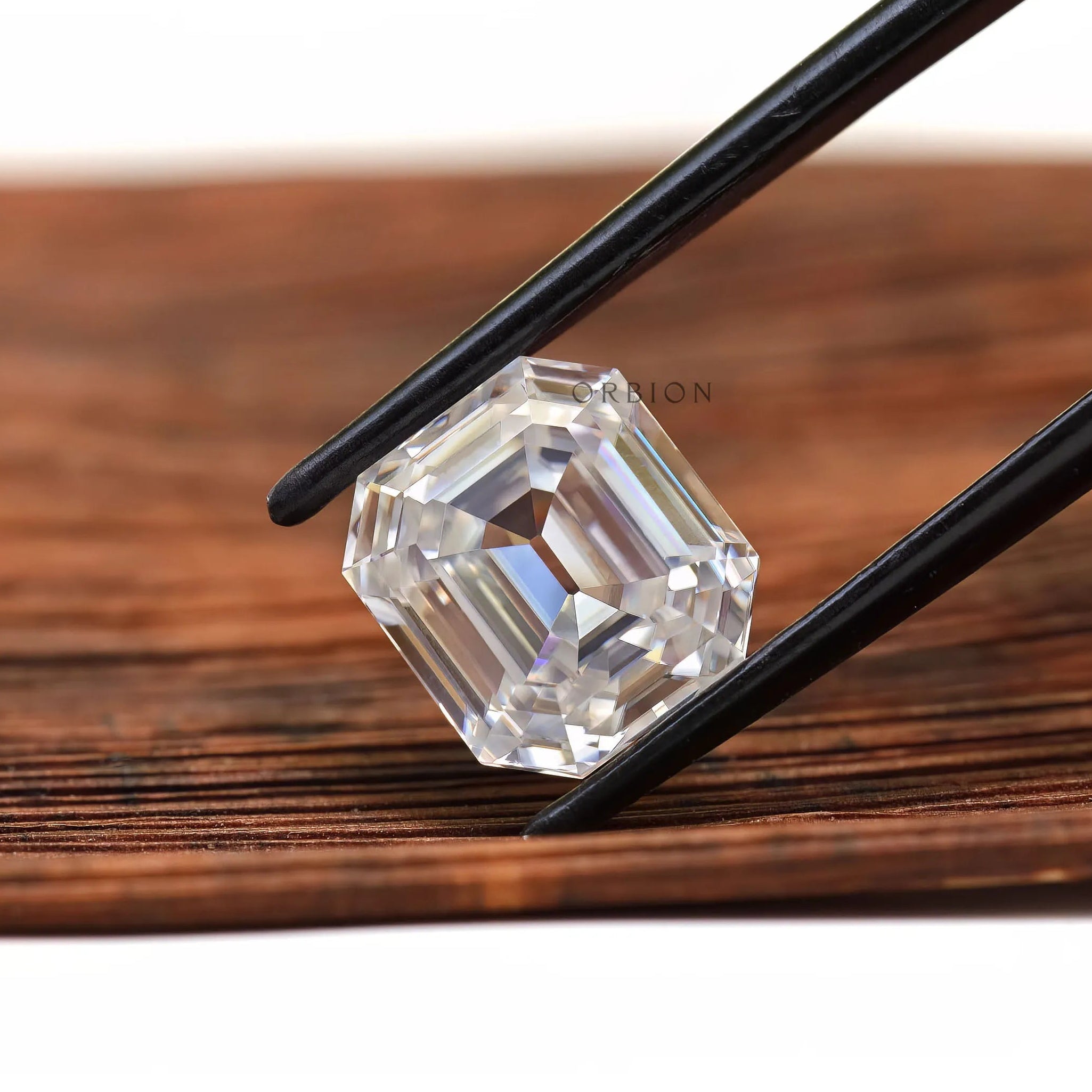 Step cut emerald moissanite shown diagonally in black tweezers