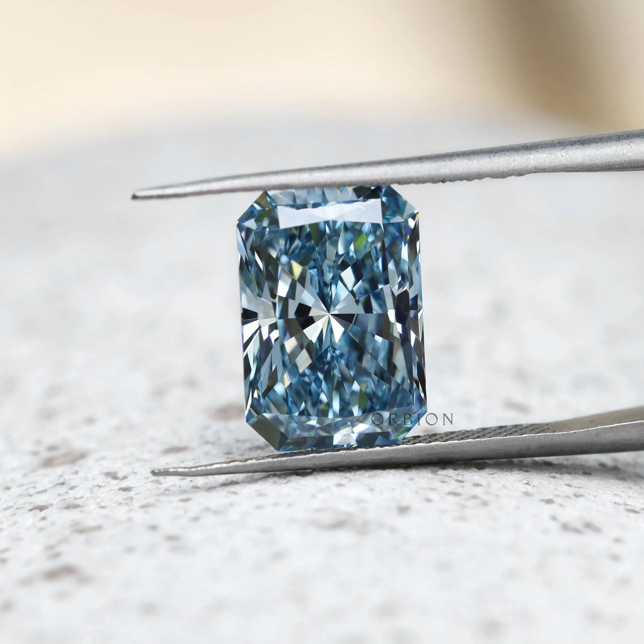 Radiant cut blue lab diamond shown upright in tweezers