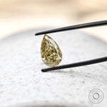 Pear shaped brownish yellow diamond over textured stone surface