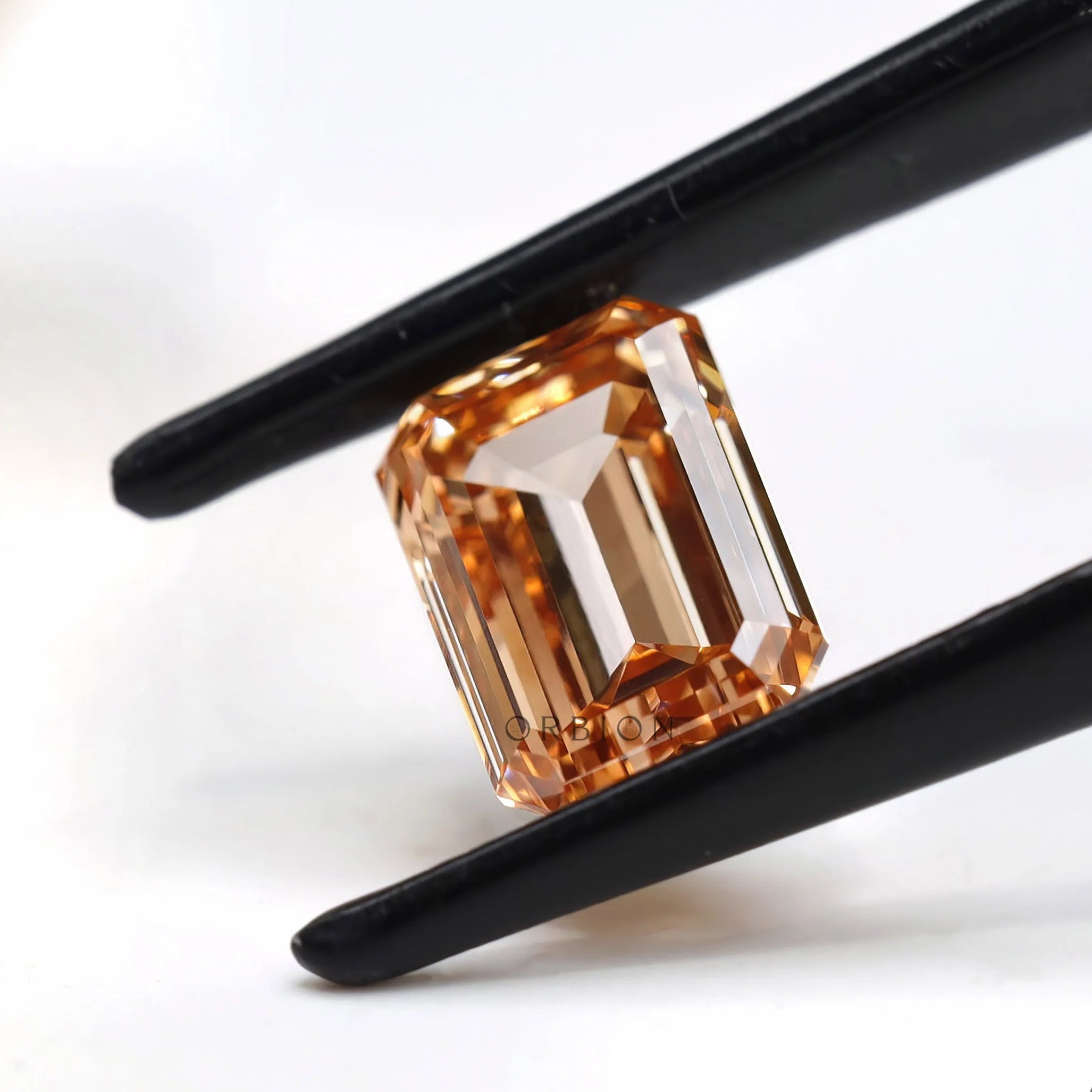 Side angled orange emerald cut diamond in tweezers