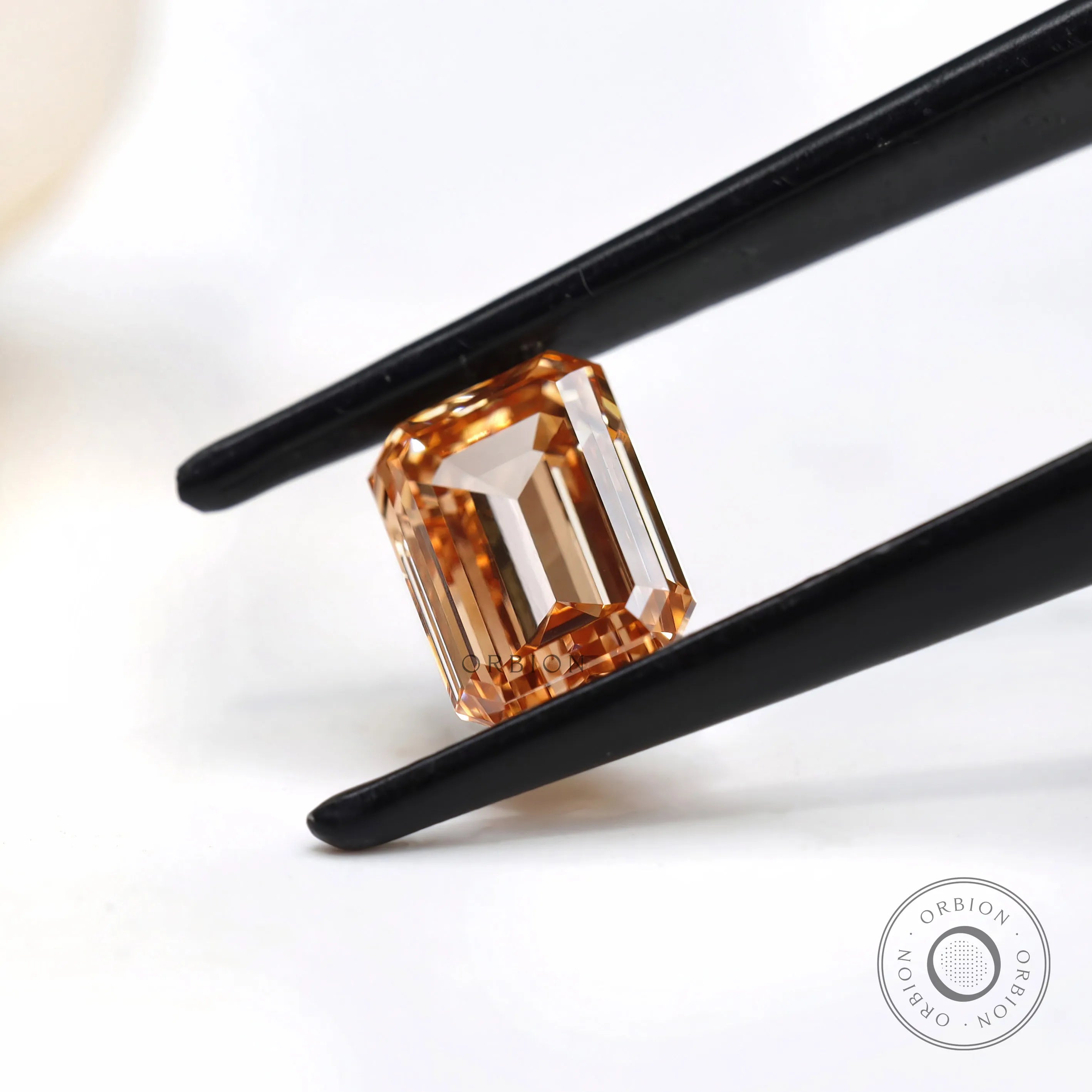 Side angled orange emerald cut diamond in tweezers