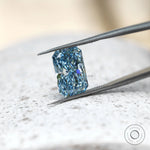 Elongated radiant blue lab diamond angled in silver tweezers