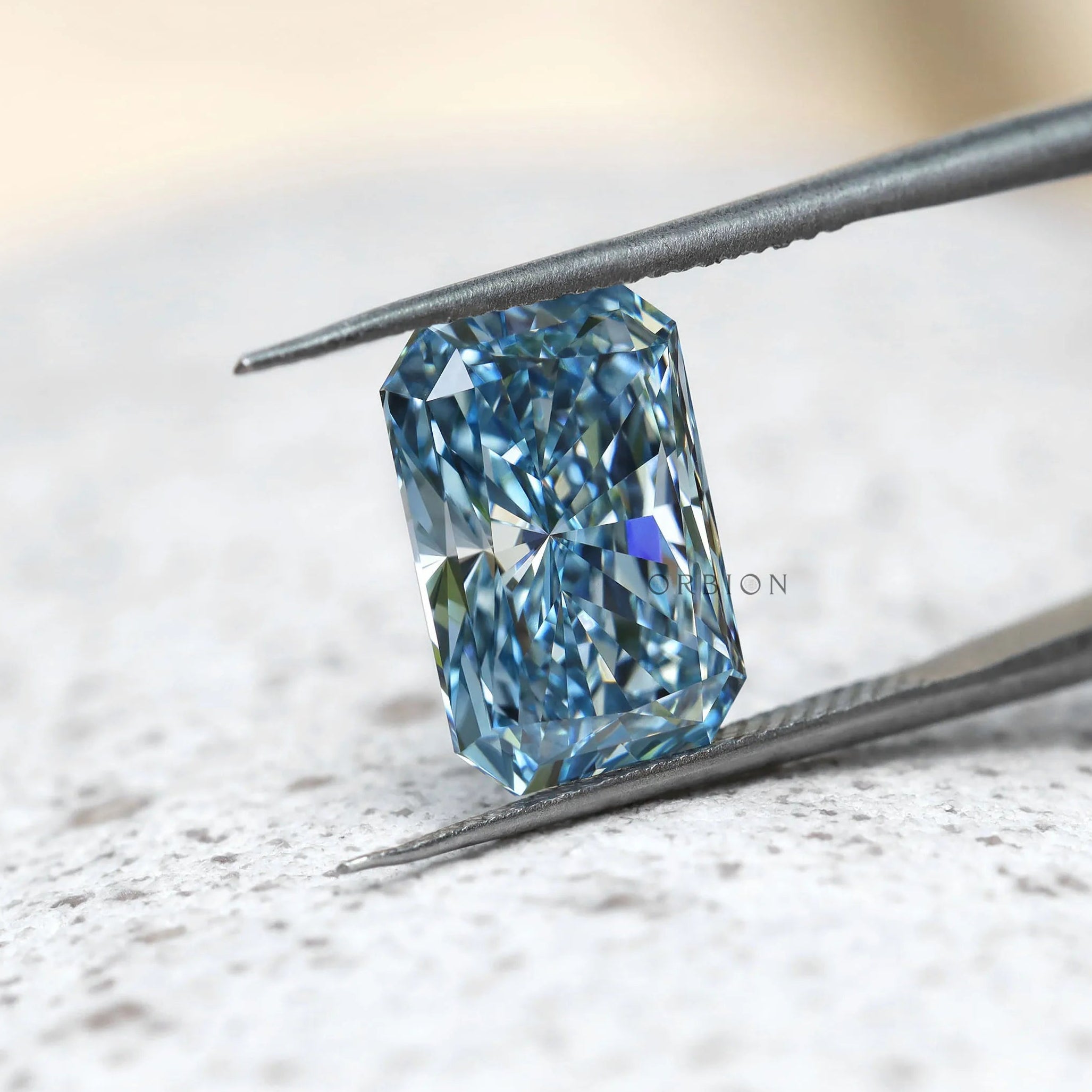 Elongated radiant blue lab diamond angled in silver tweezers